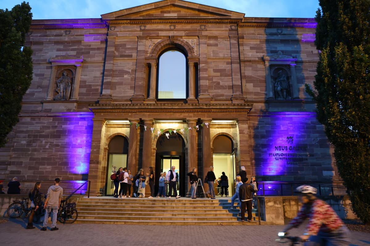 Young people chat and stand together in front of the illuminated museum building.