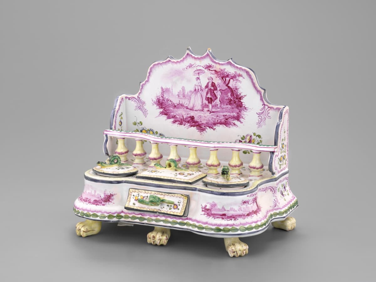 Verziertes Tintenfass aus Porzellan mit rosa pastoralen Szenen, Kerzenhaltern und Löwentatzenfüßen auf grauem Hintergrund.