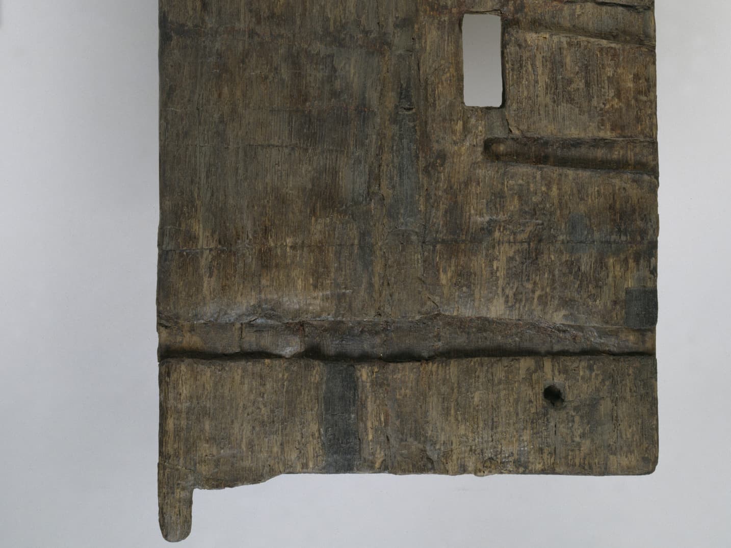Nahaufnahme eines antiken Holzartefakts mit rechteckigem Ausschnitt und sichtbarer Maserung vor einem schlichten Hintergrund.
