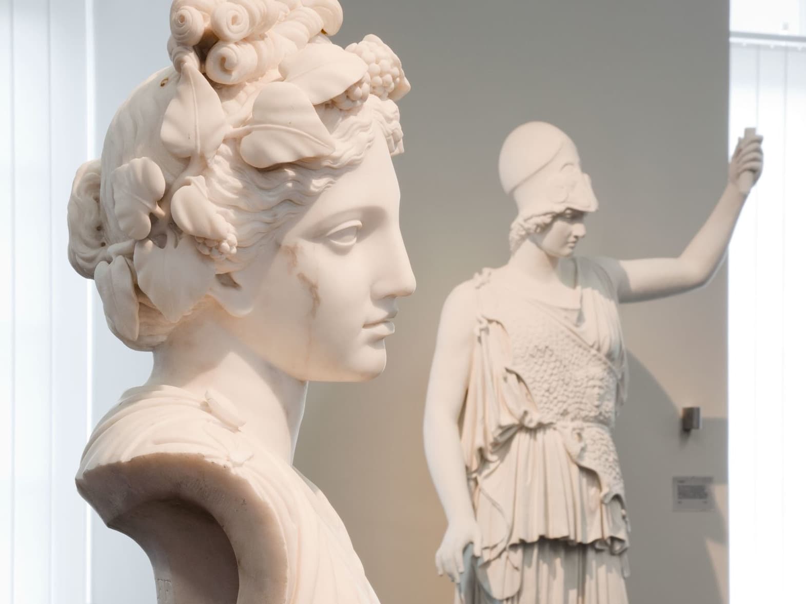 Marmorbüste einer Frau im Vordergrund, im Hintergrund die Statue einer Frau in Rüstung, die einen Speer hält.