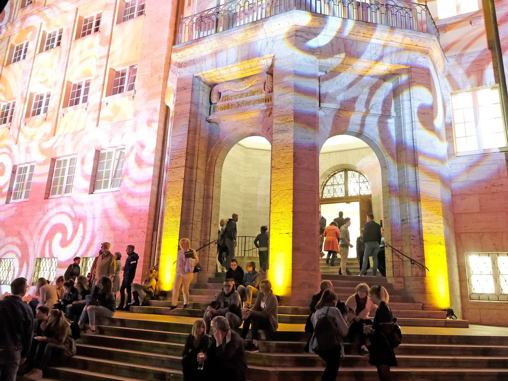 Besuchergruppen vor farbig beleuchtetem Hessischen Landesmuseum.