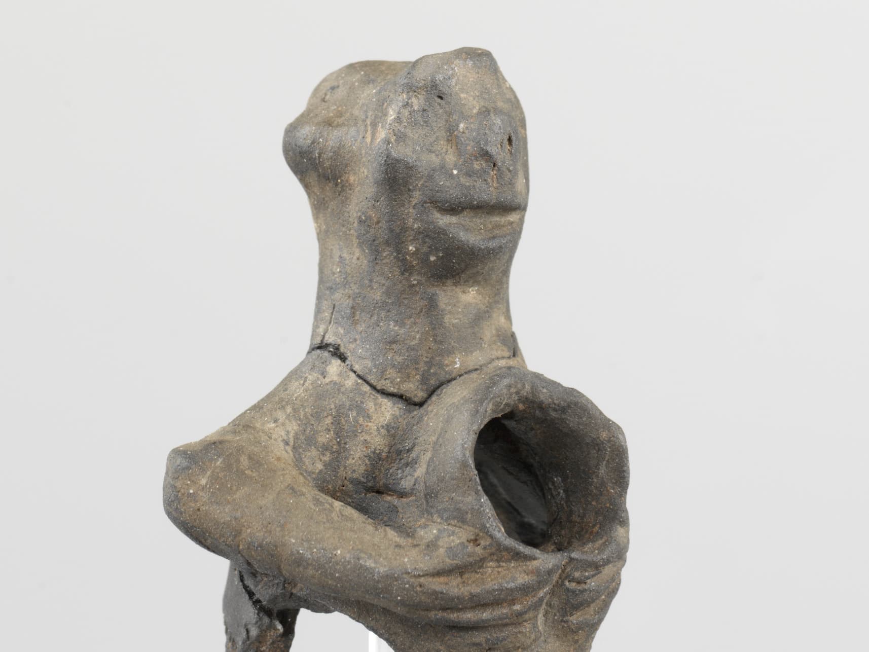 Antike Tonfigur mit hohlem Körper und einfachen menschenähnlichen Gesichtszügen, darunter ein runder Kopf und subtile Gesichtsdetails.