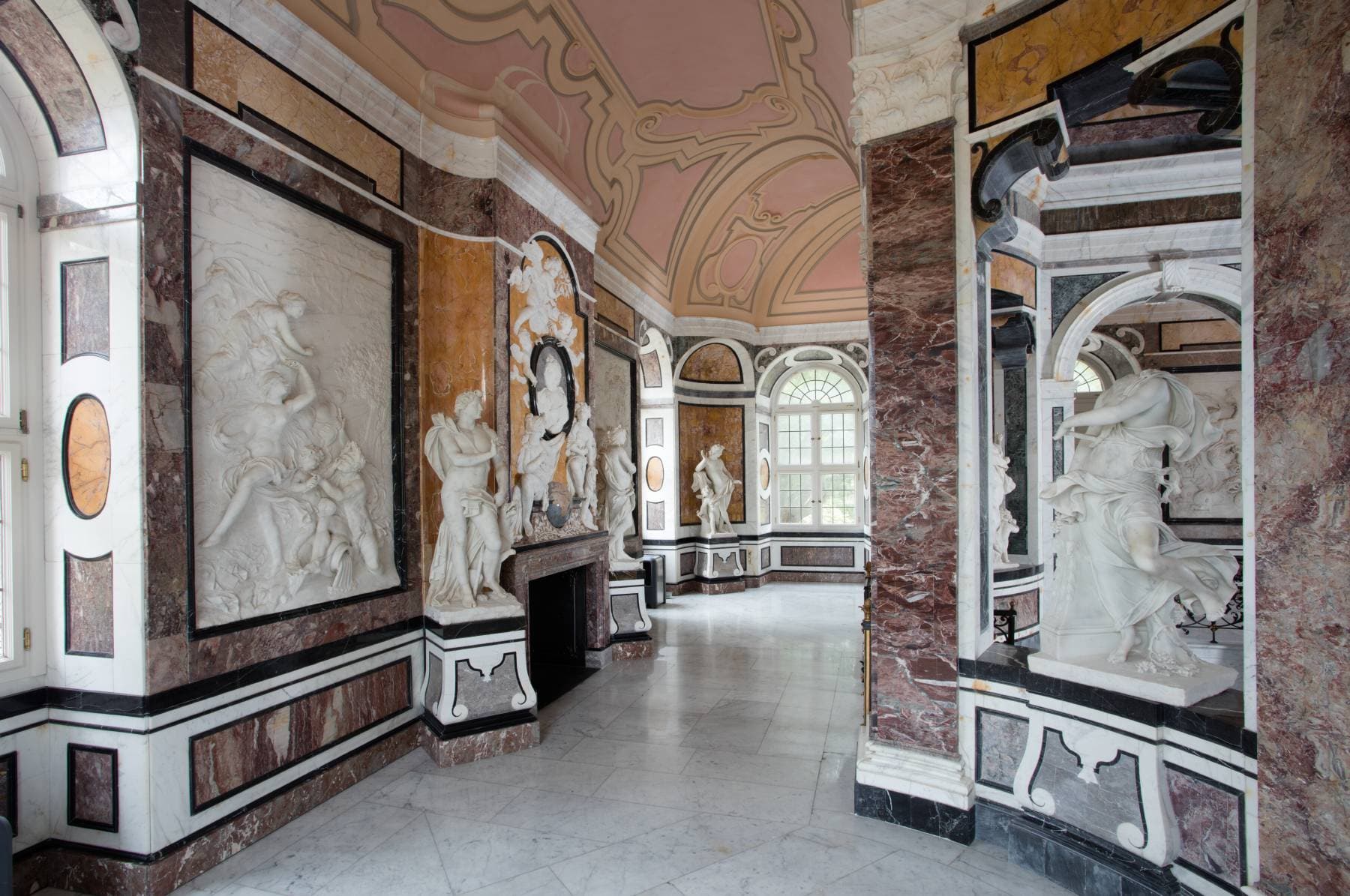 Ornate room with marble statues, intricate ceiling designs, large windows, and detailed wall carvings, creating a grand and elegant atmosphere.