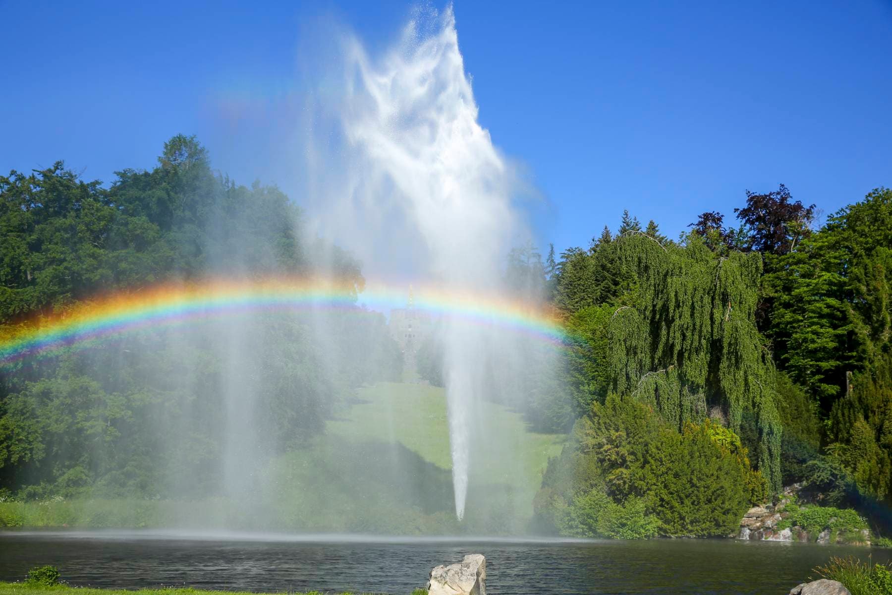 Große Fontäne, die einen Regenbogen hervorbringt, eingebettet in den grünen Bergpark.