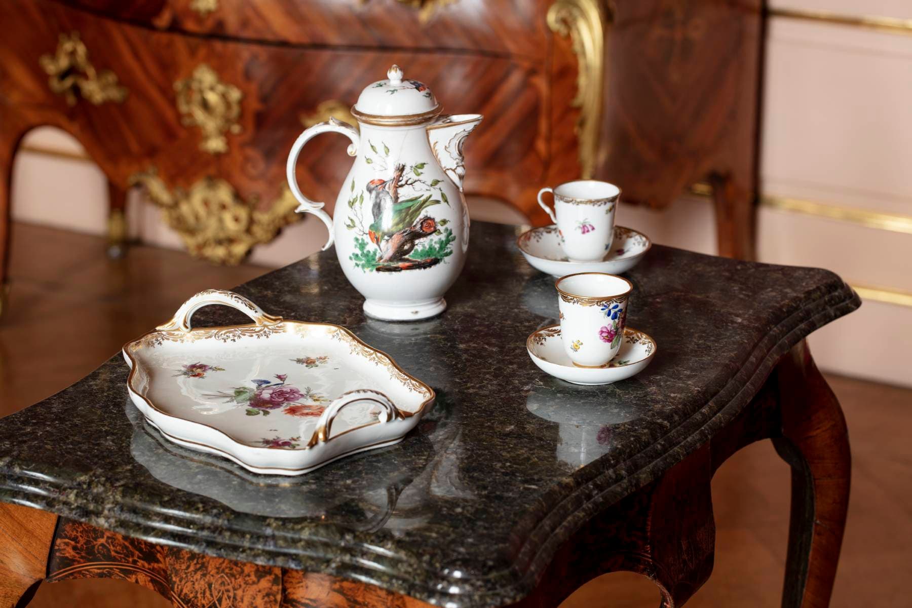 Elegantes Teeservice aus Porzellan mit Blumenmuster auf einem dunklen Marmortisch, bestehend aus einer Teekanne, zwei Tassen mit Untertassen und einem Tablett.