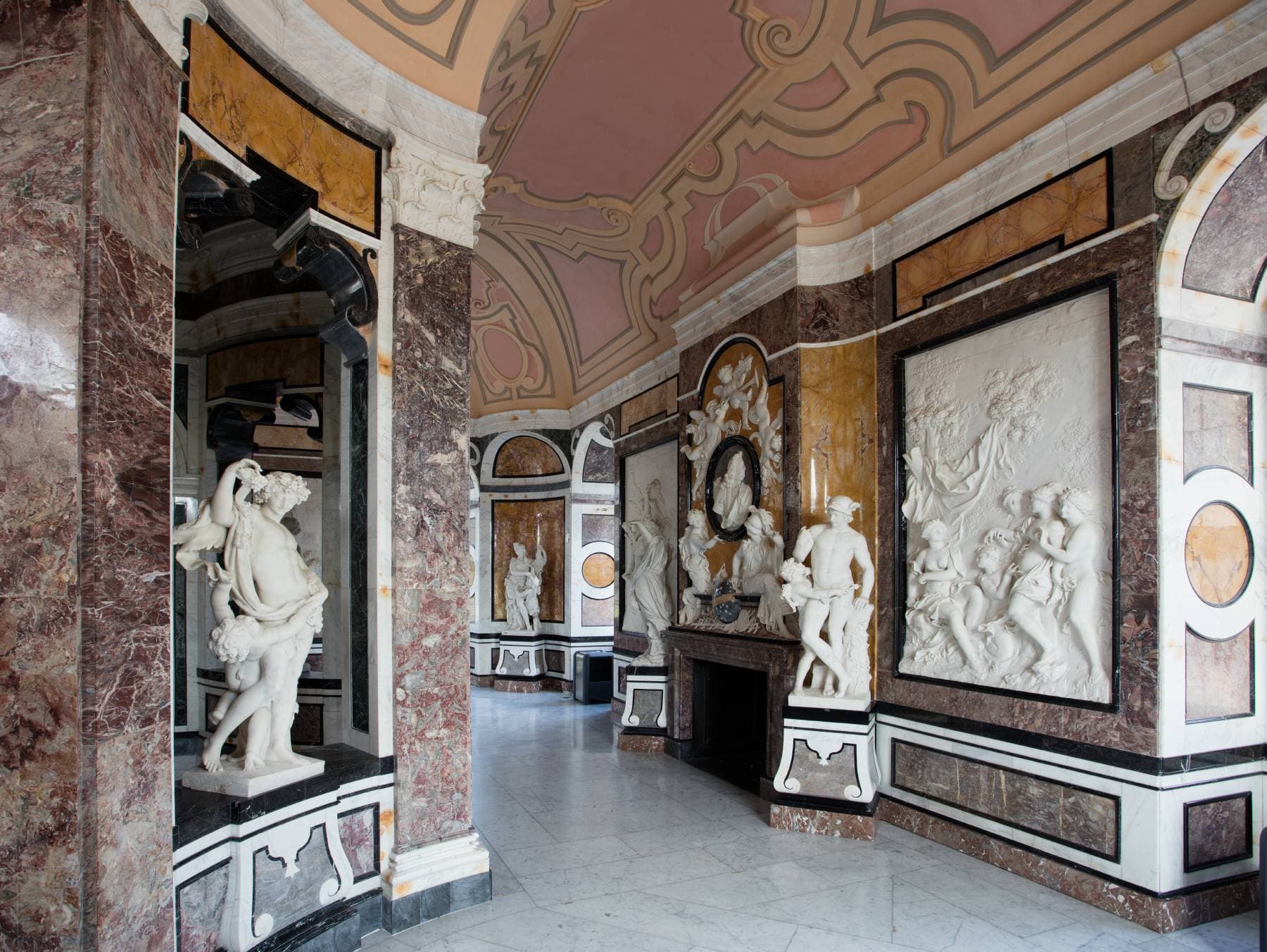 Reich verzierter Raum mit Marmorstatuen, aufwendigen Wandschnitzereien und einer dekorativen Decke mit klassischen Figuren und eleganten architektonischen Details.