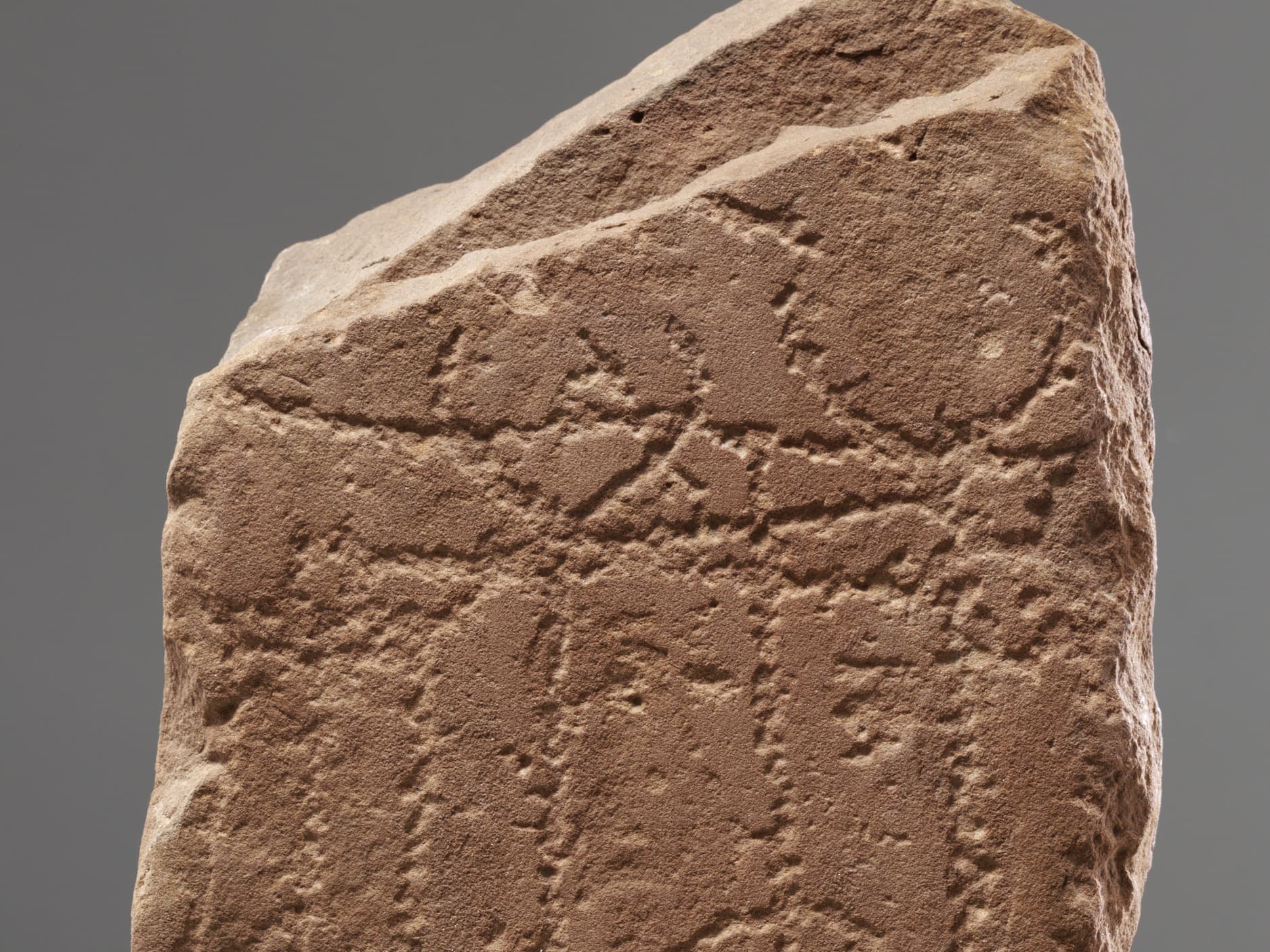 Nahaufnahme einer alten Steintafel mit verwitterter Oberfläche und schwachen Inschriften vor neutralem Hintergrund.