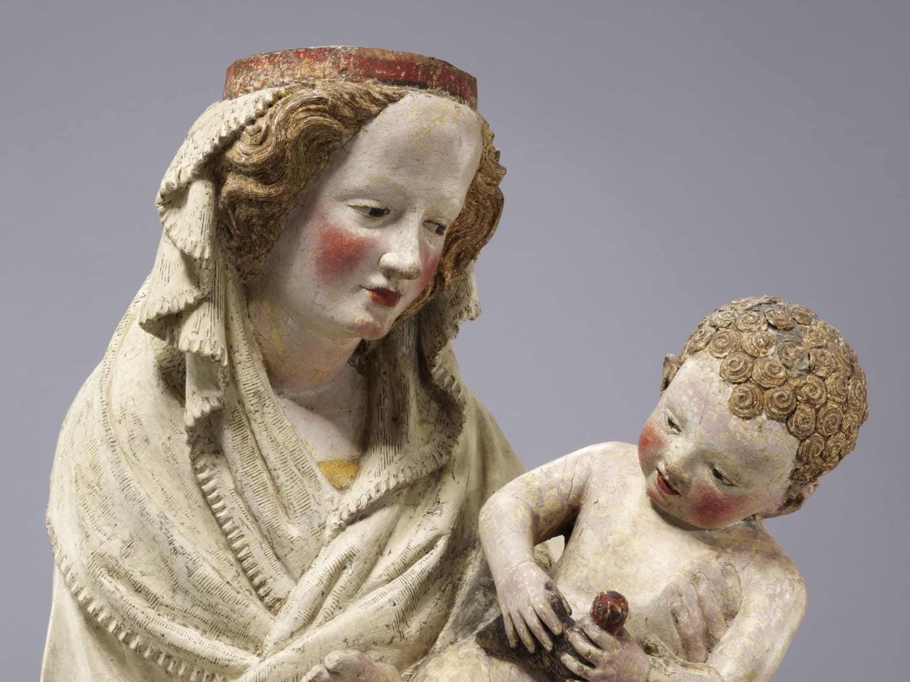 Mittelalterliche Skulptur einer Frau mit Schleier, die ein Kind hält, beide mit detailliertem Gesichtsausdruck und rosigen Wangen.