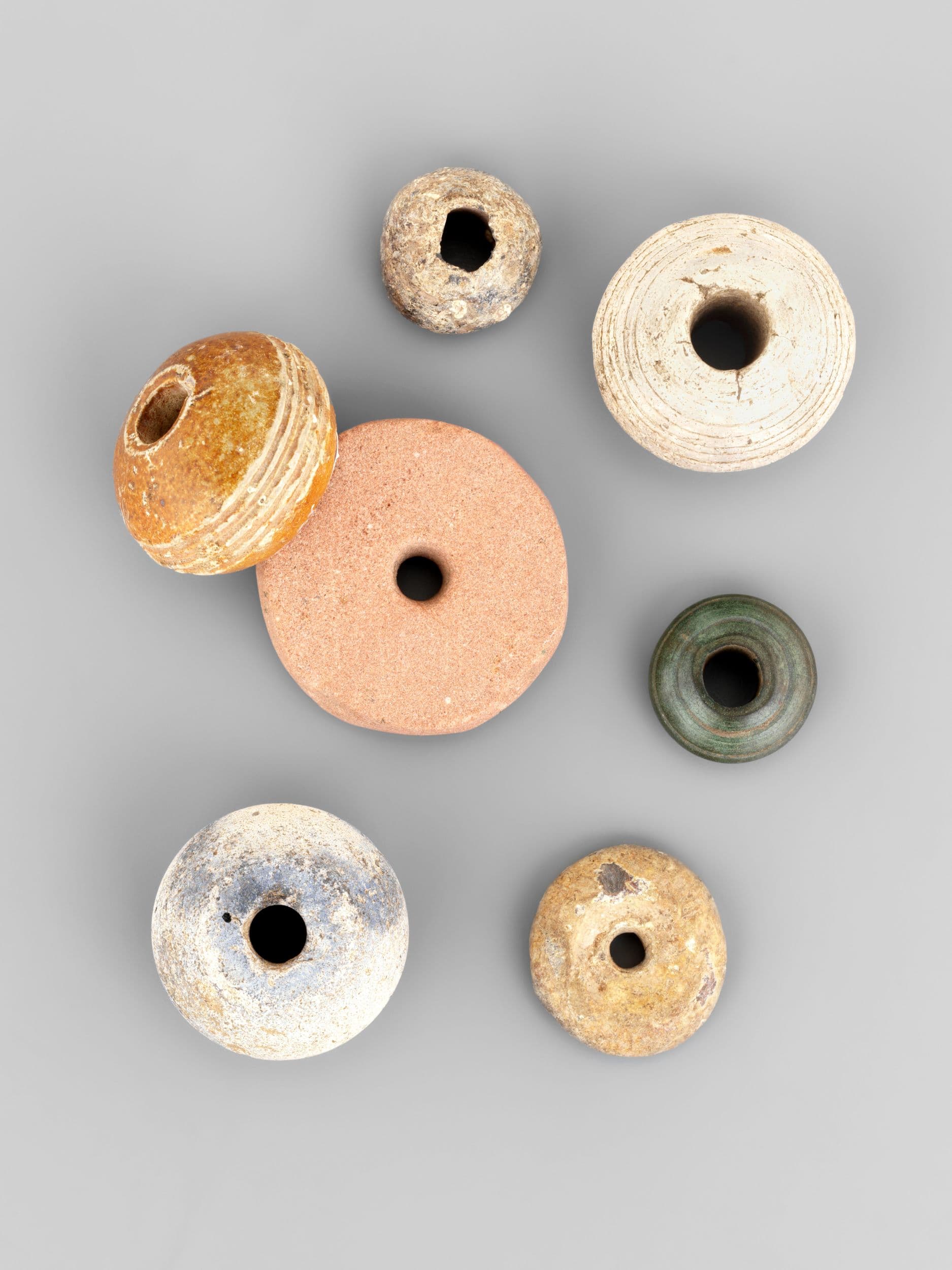 Seven assorted clay and stone beads of various colors and sizes arranged on a gray background.
