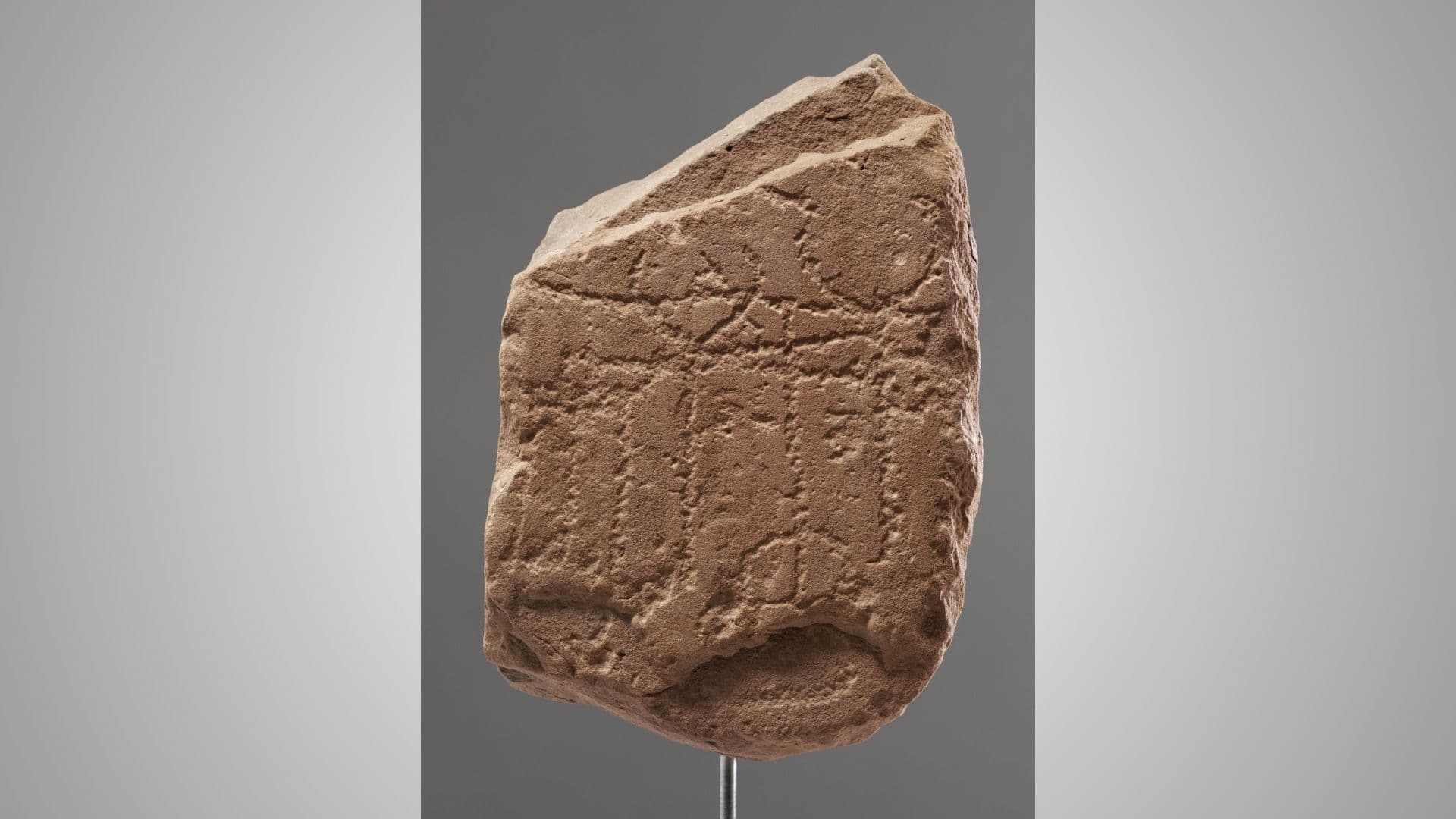 A weathered stone slab with ancient carvings, featuring geometric shapes and lines, displayed against a neutral background.