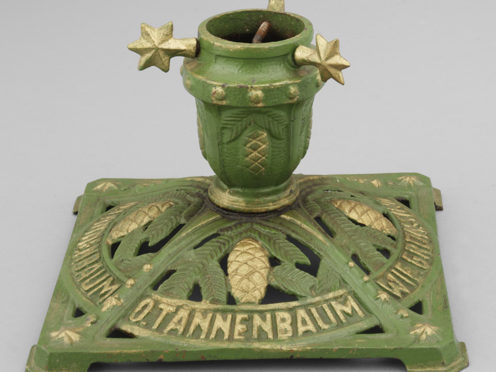 Vintage green and gold metal Christmas tree stand with pinecone design and "O Tannenbaum" inscription.