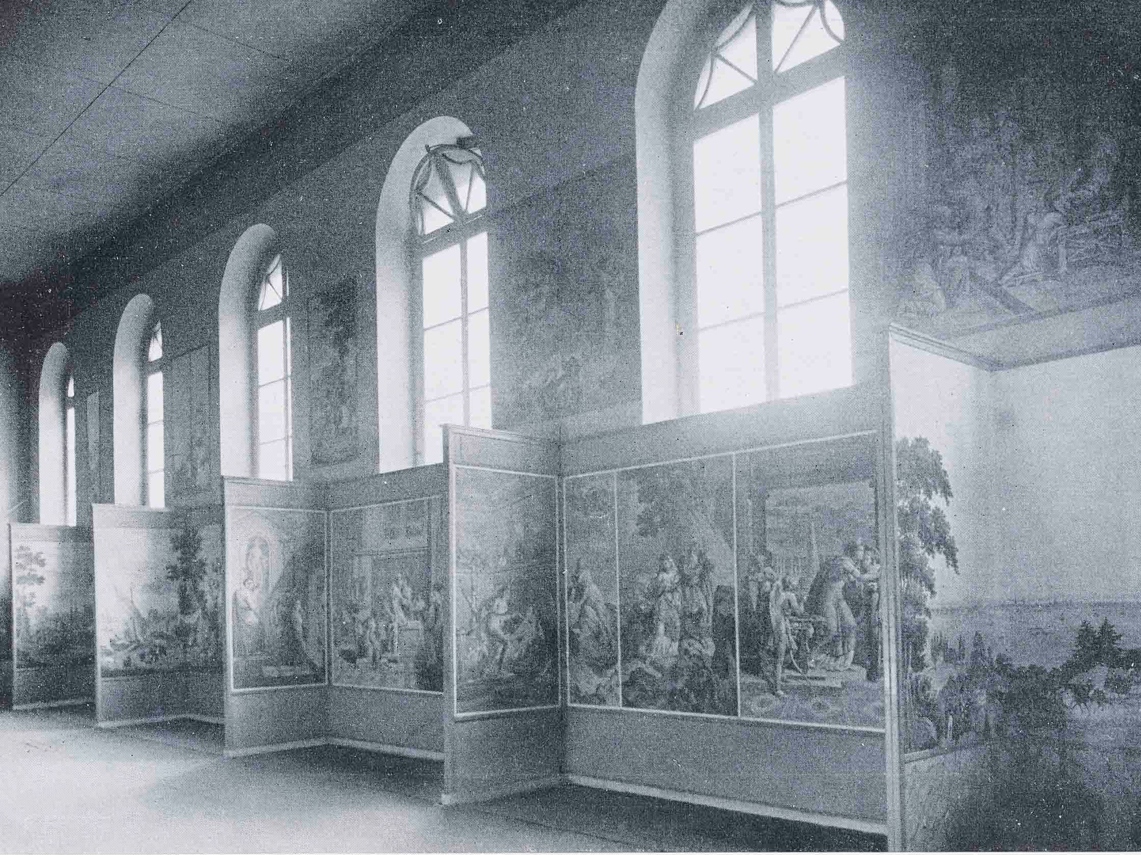 in einer Galerie mit hohen Bogenfenstern sind große, detaillierte Gemälde auf unterteilten Tafeln ausgestellt, die verschiedene historische Szenen darstellen.