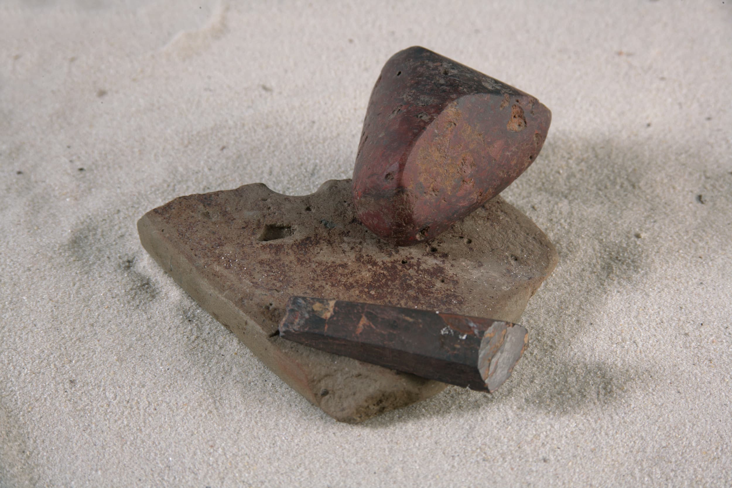 Ancient stone tools on sand, featuring a polished axe head and a chisel-like tool.