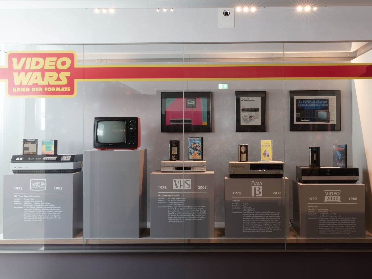 Ausstellung zur Entwicklung der Videoformate, darunter VCR, VHS, Betamax und Video 2000, mit beschreibenden Tafeln und Vintage-Fernsehern.