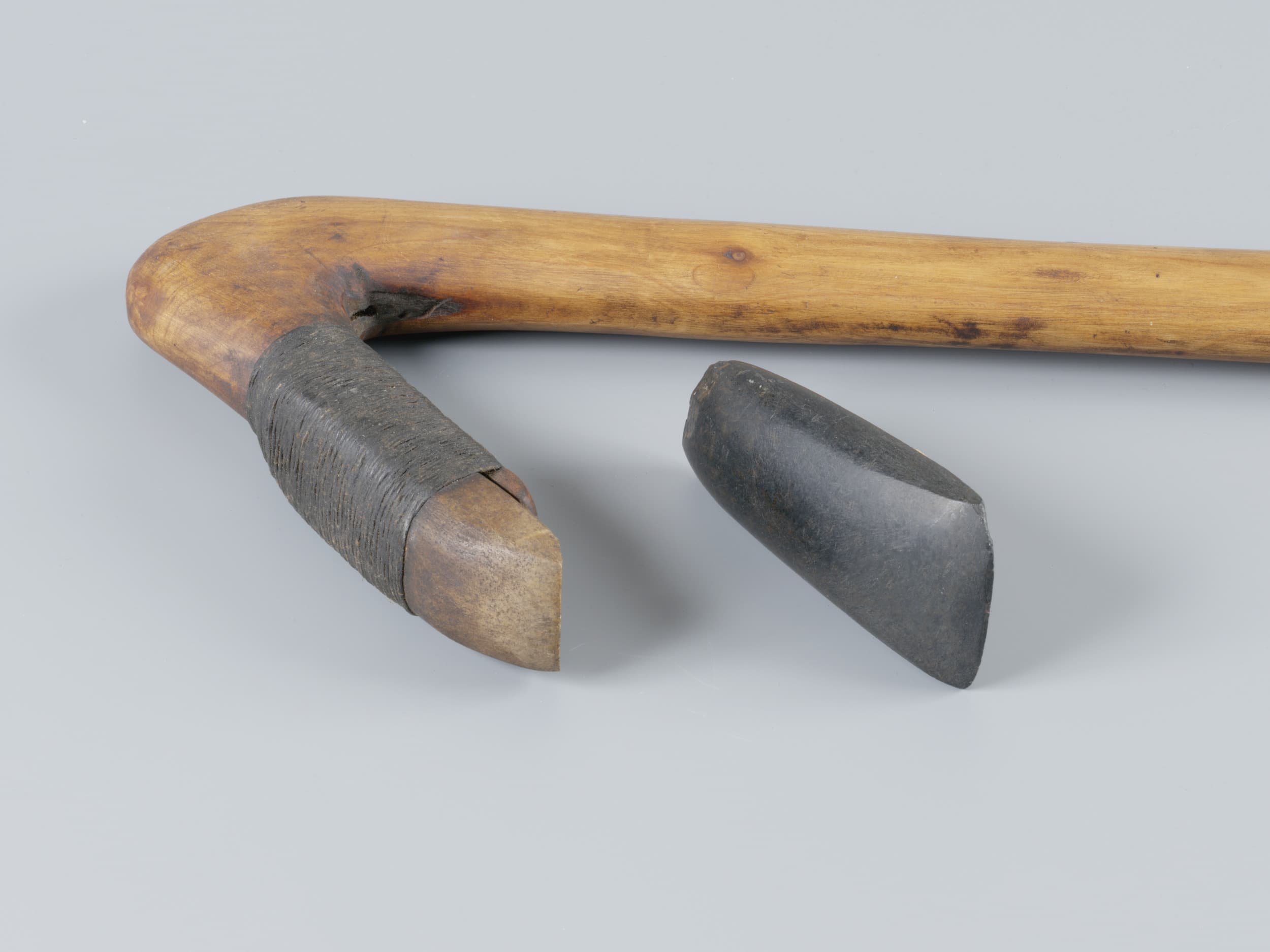 Wooden tool handle with a stone blade, showing a wrapped joint for attachment. The blade is detached and placed beside the handle.