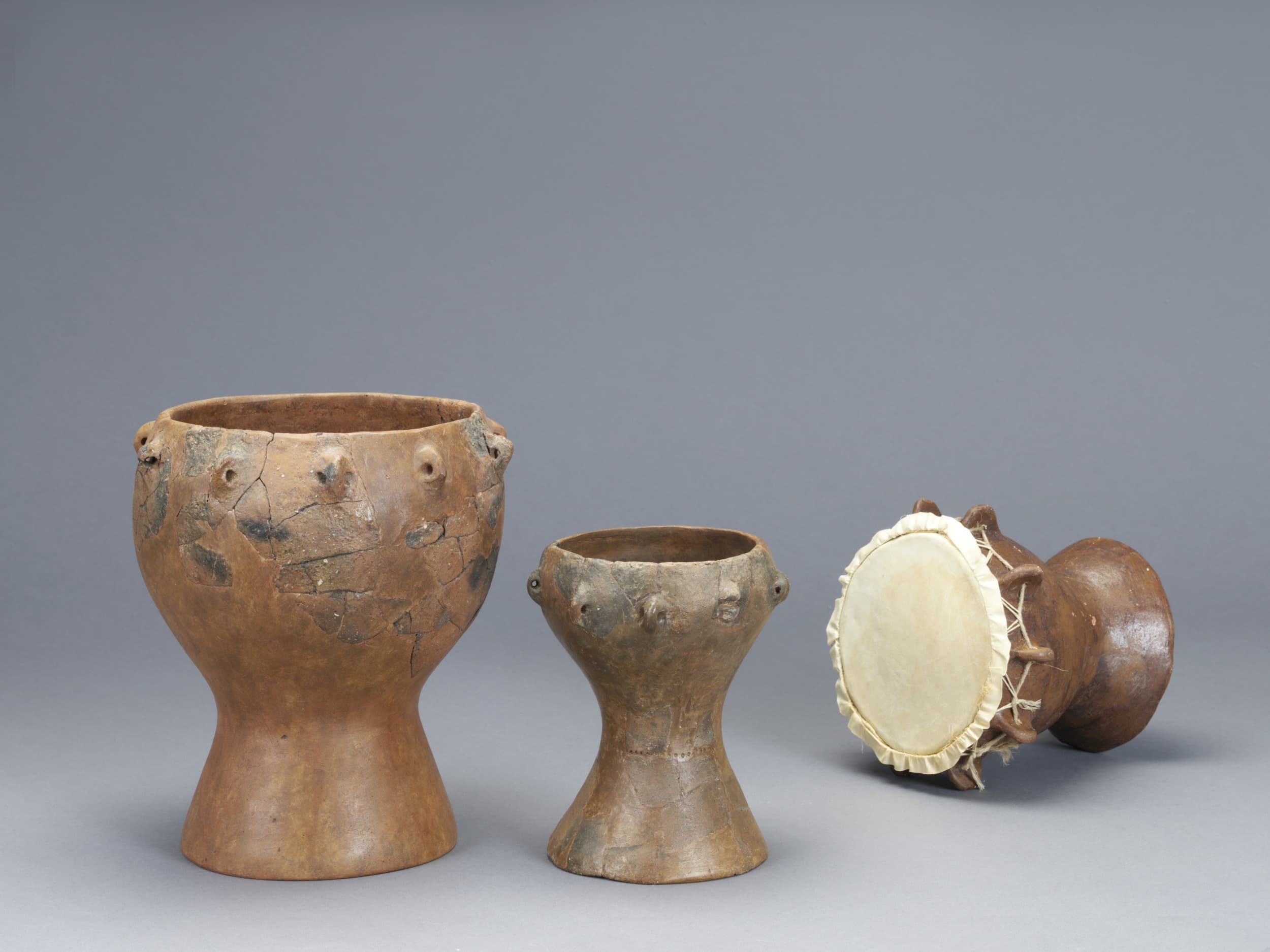 Three traditional clay drums with varying sizes and shapes, featuring a natural finish and visible texture, displayed on a neutral background.