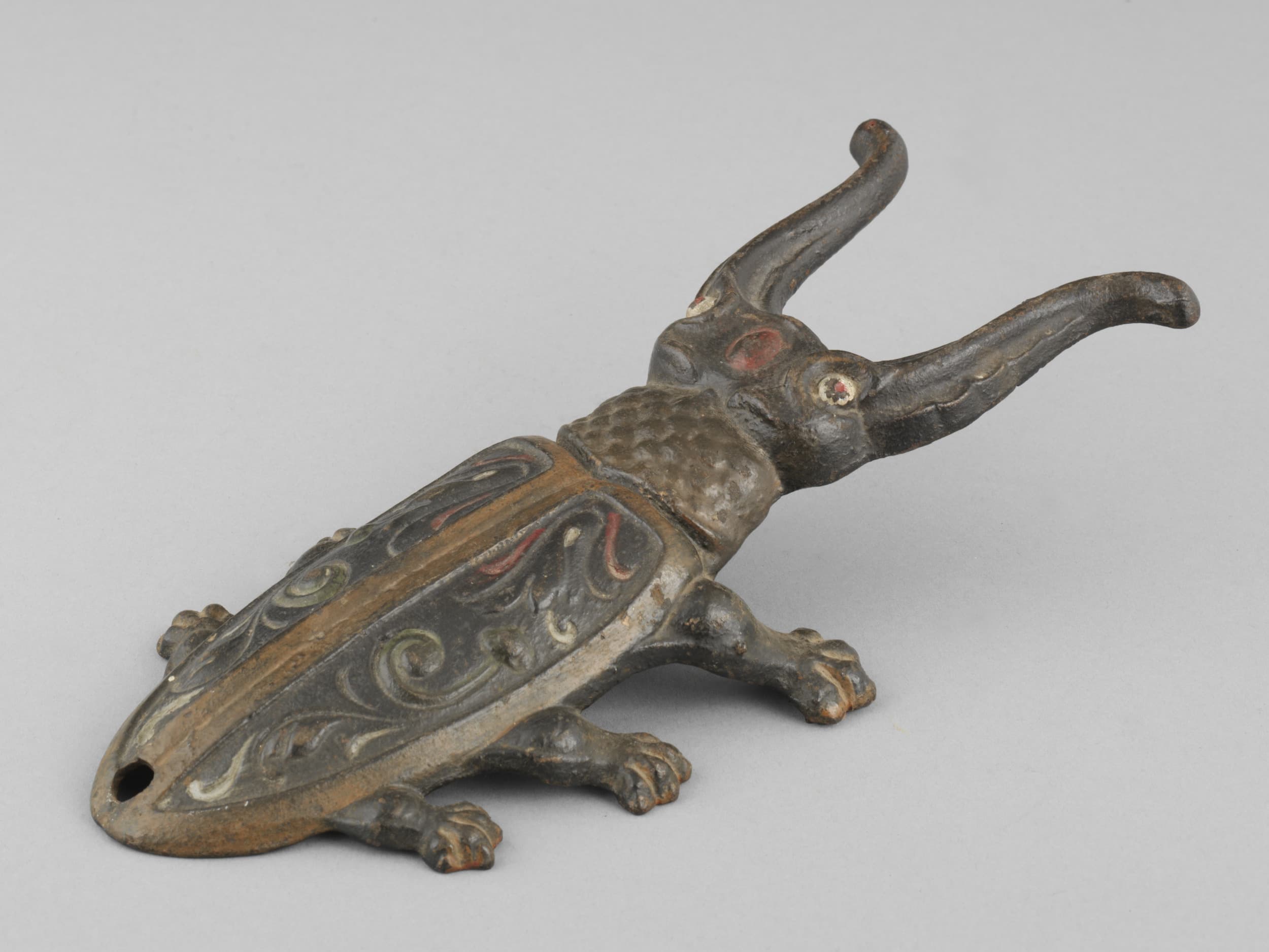 Bronzeskulptur eines Käfers mit kunstvollen Details und langen, gebogenen Hörnern vor einem schlichten grauen Hintergrund.