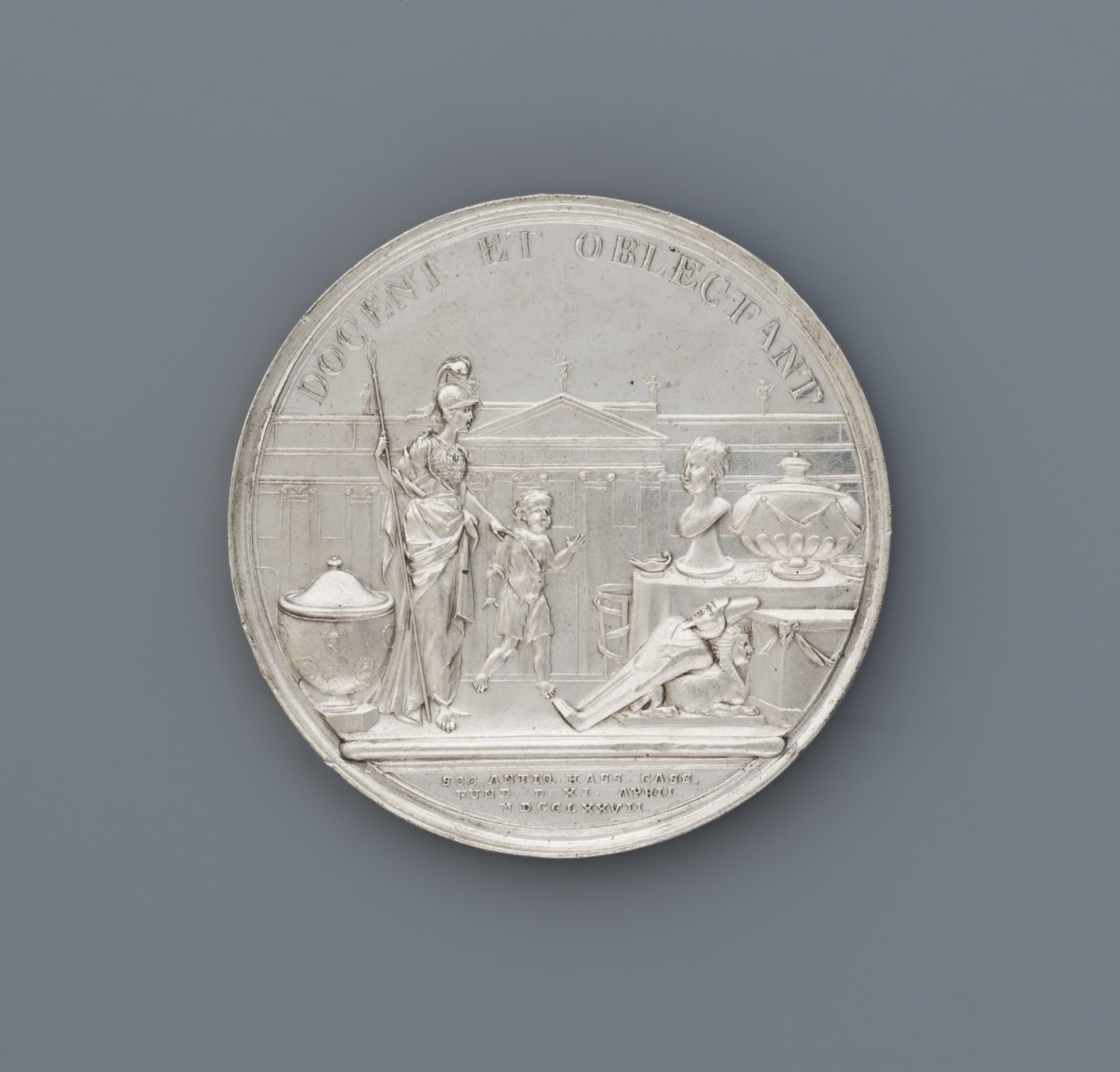 Silbermedaille mit der Darstellung einer allegorischen Szene mit Figuren, darunter eine Frau und Kinder, umgeben von klassischen Elementen und eingraviertem Text.