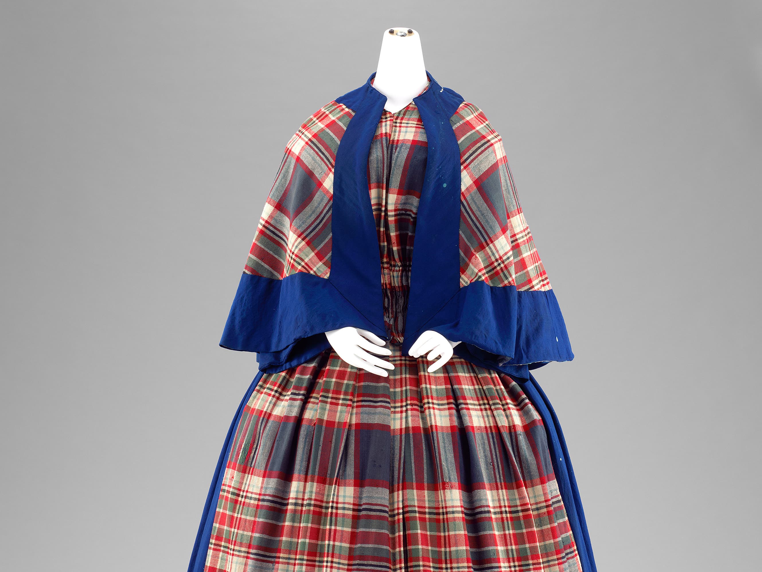 Ausschnitt eines  2-teiligen Kleides mit Pelerine aus kariertem Wollstoff mit blauen Garnituren