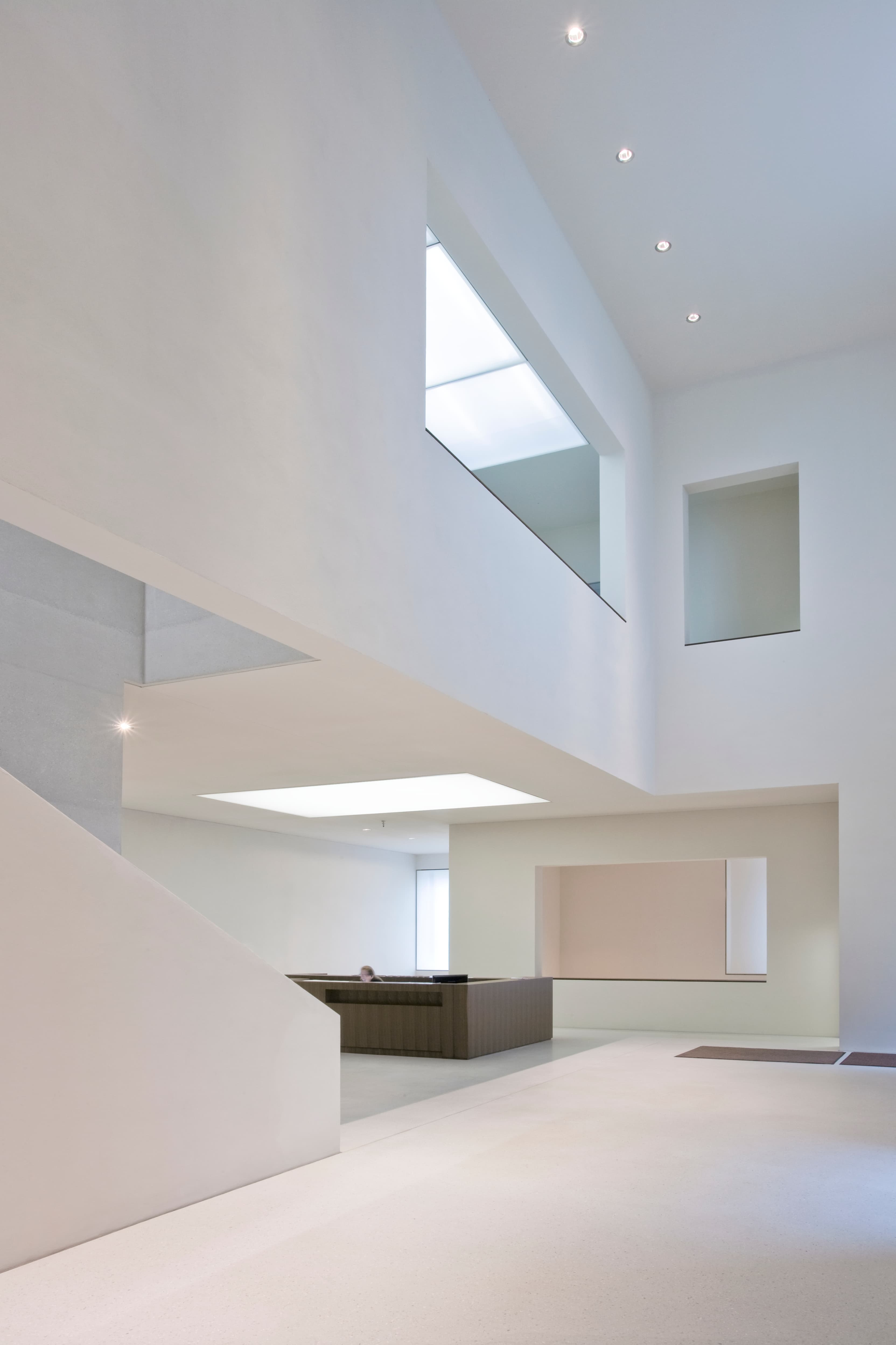 Minimalistisches Interieur mit hohen Decken, weißen Wänden, großen Fenstern und einer modernen Treppe. Natürliches Licht erhellt den offenen Raum.