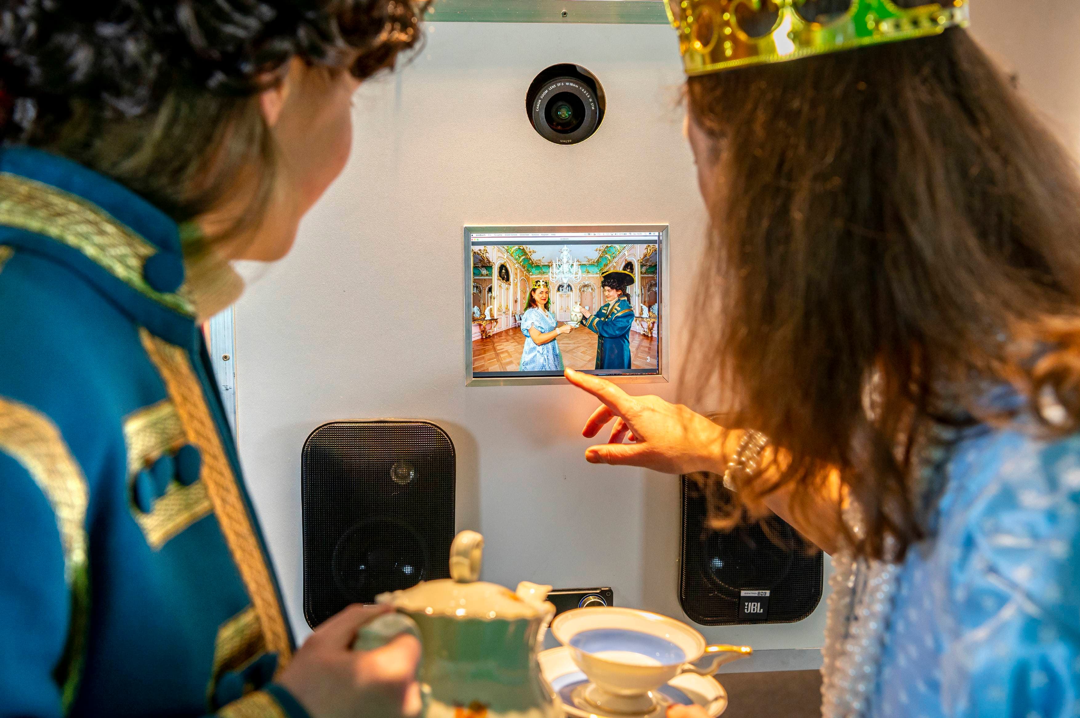 Two people in costumes look at a screen showing them in Wilhelmsthal Castle.
