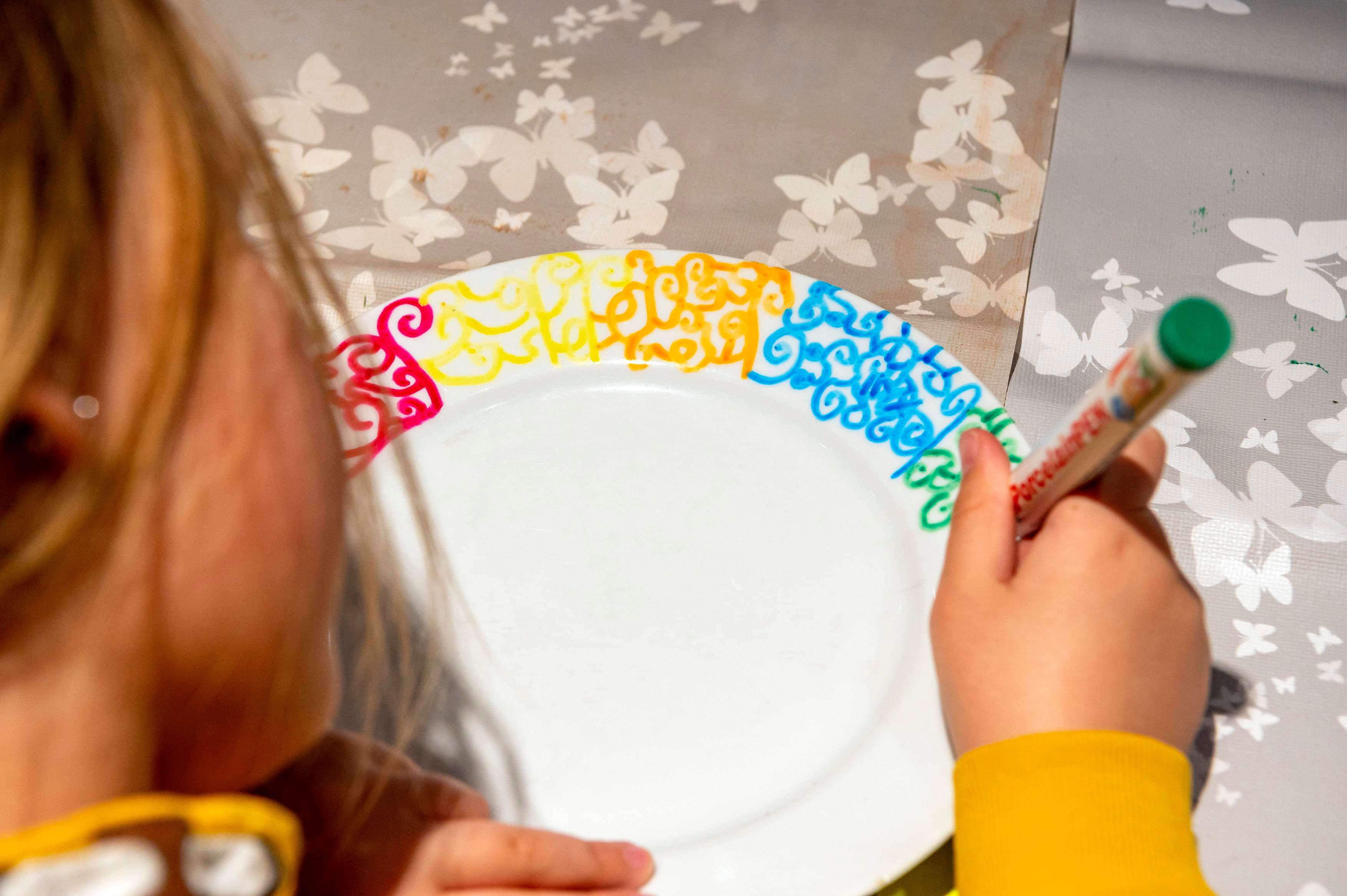 Child paints the brim of a white plate.