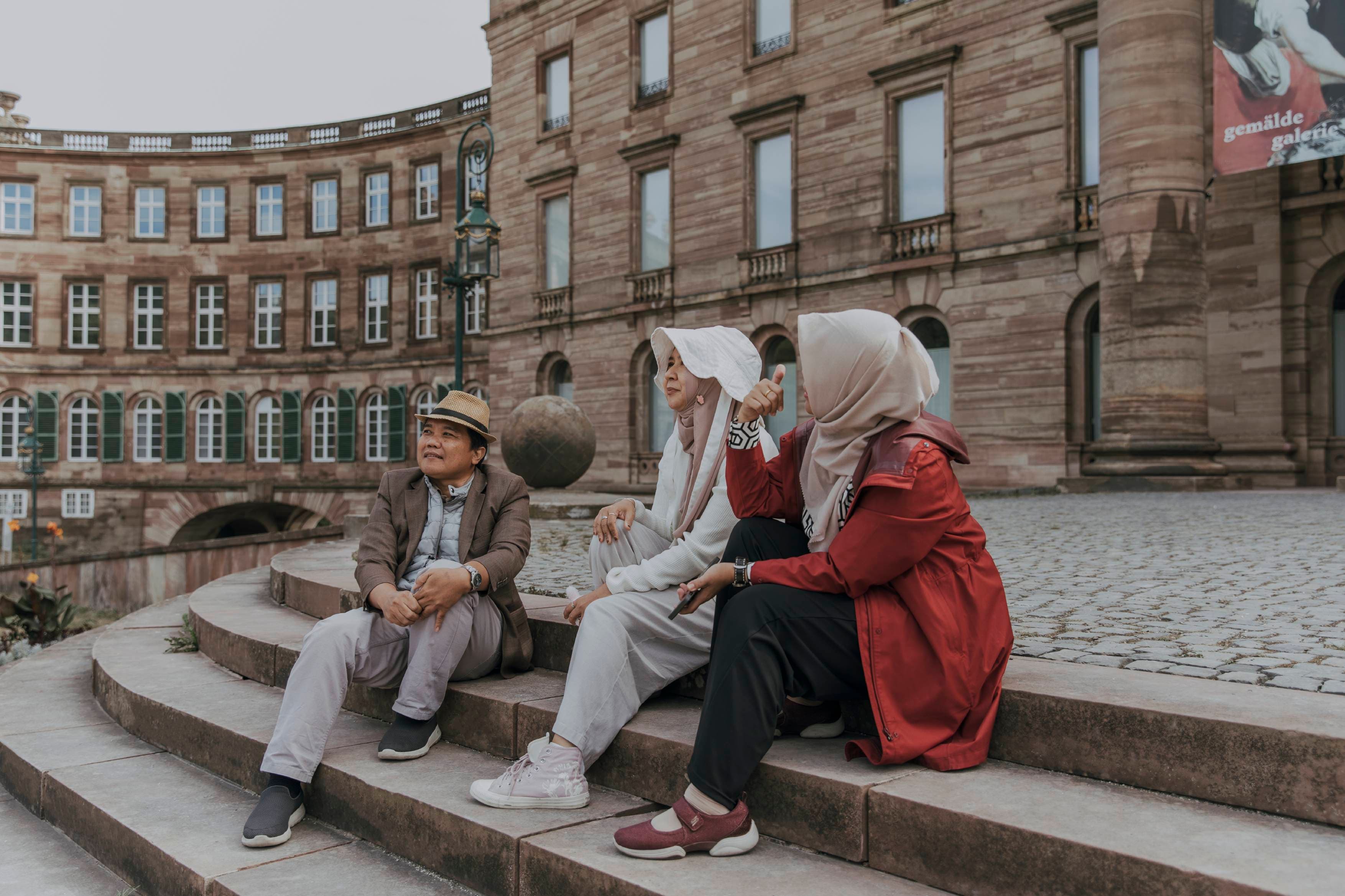 Drei Menschen sitzen auf Treppenstufen vor Schloss Wilhelmshöhe.