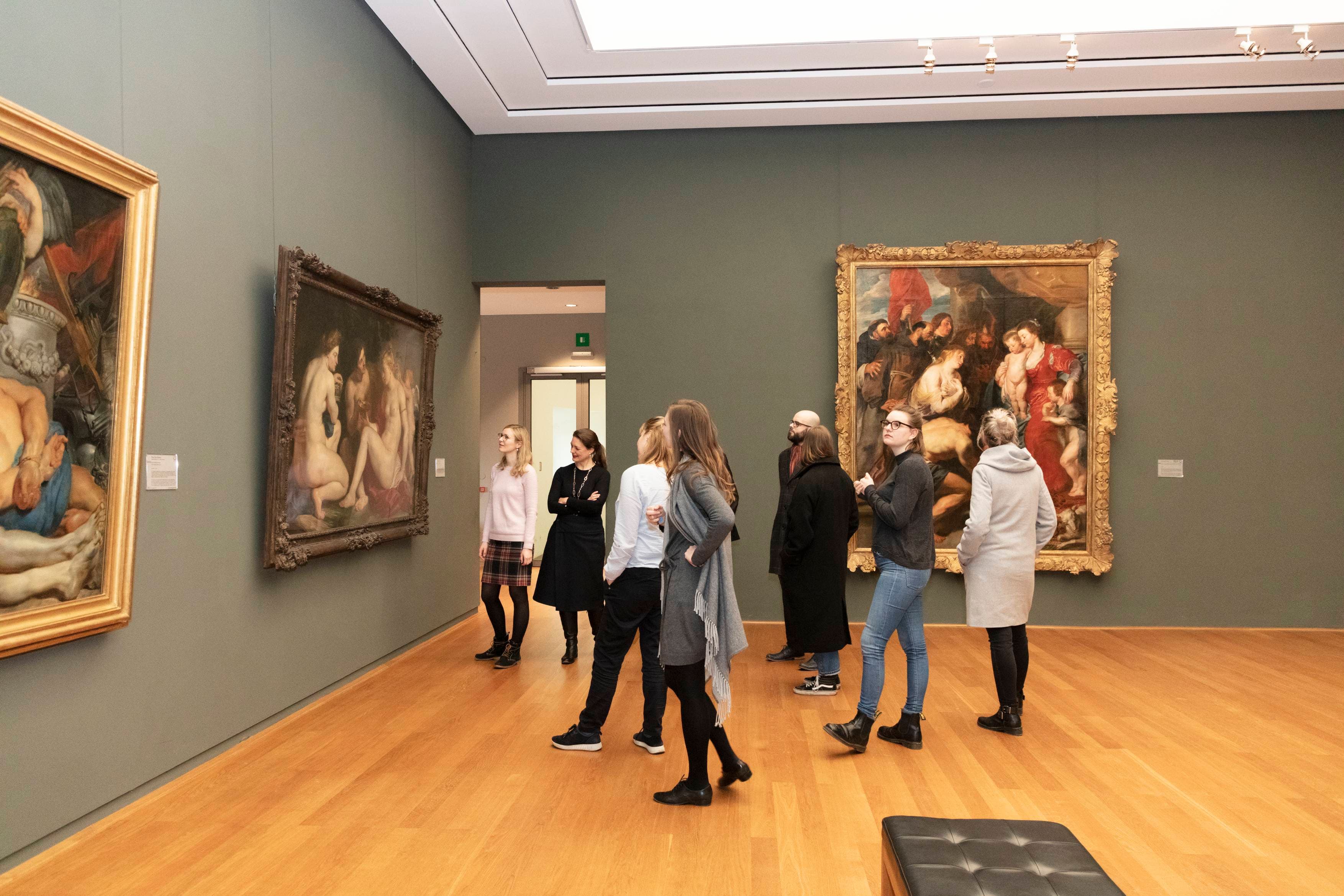 Menschen betrachten große Gemälde in einer Kunstgalerie mit Holzböden und sanfter Beleuchtung.