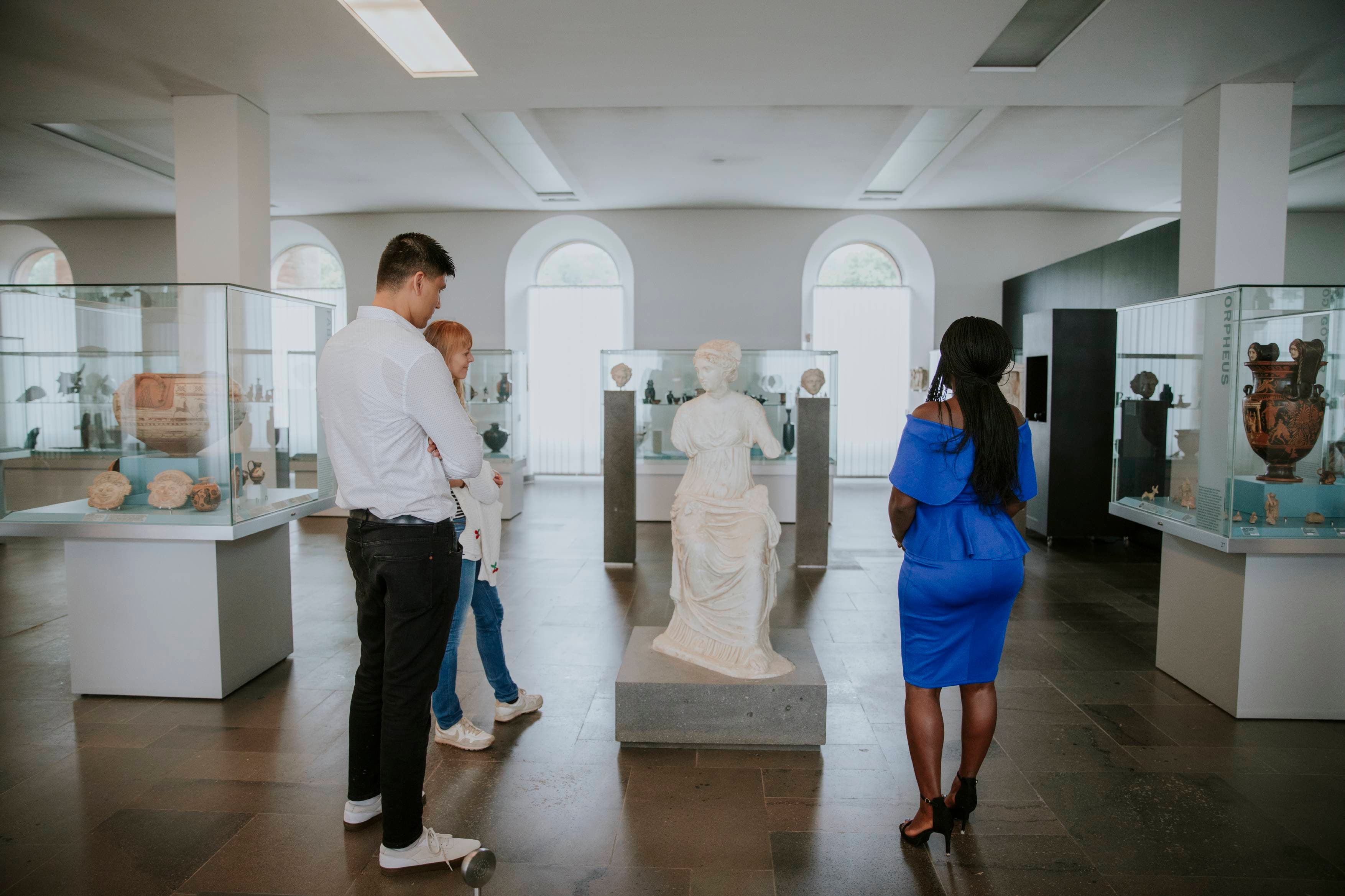 Drei Gäste der Antikensammlung betrachten eine sitzende Marmorskulptur