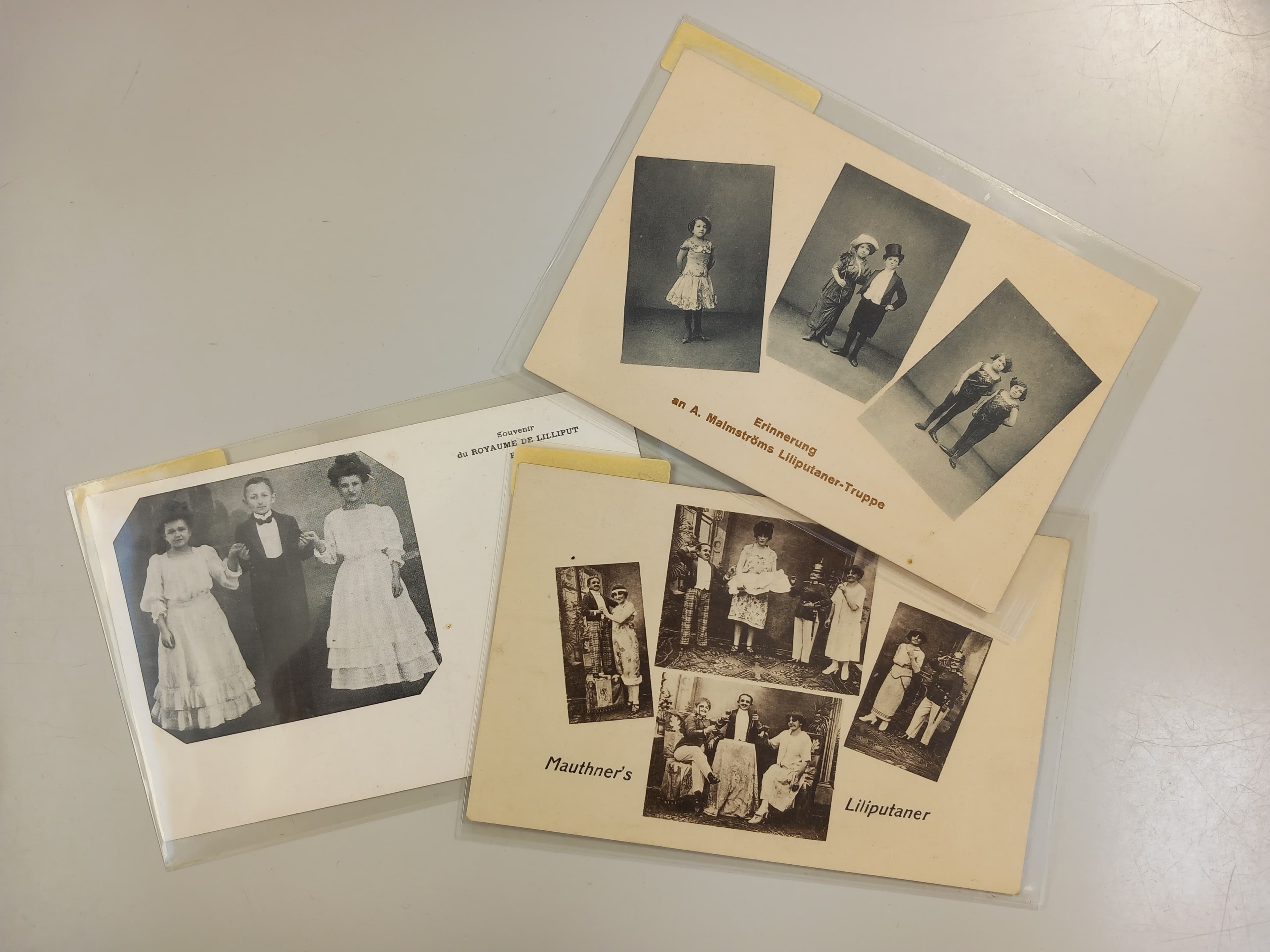 Auf einem Tisch liegen drei Vintage-Fotokarten, die jeweils Schwarzweißporträts von Menschen in zeitgenössischer Kleidung zeigen.