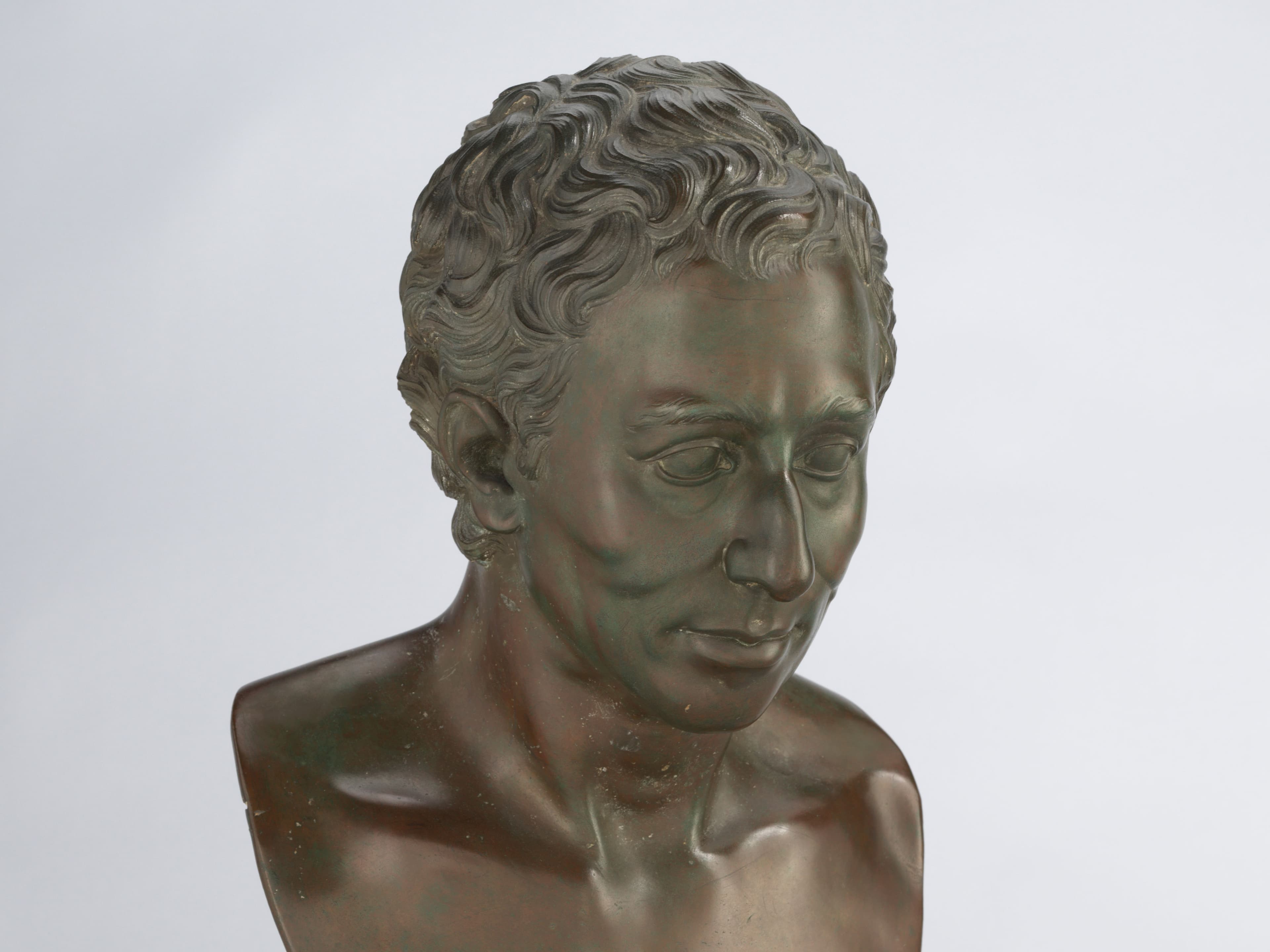 Bronzebüste eines Mannes mit lockigem Haar auf einem Marmorsockel vor einem schlichten Hintergrund.