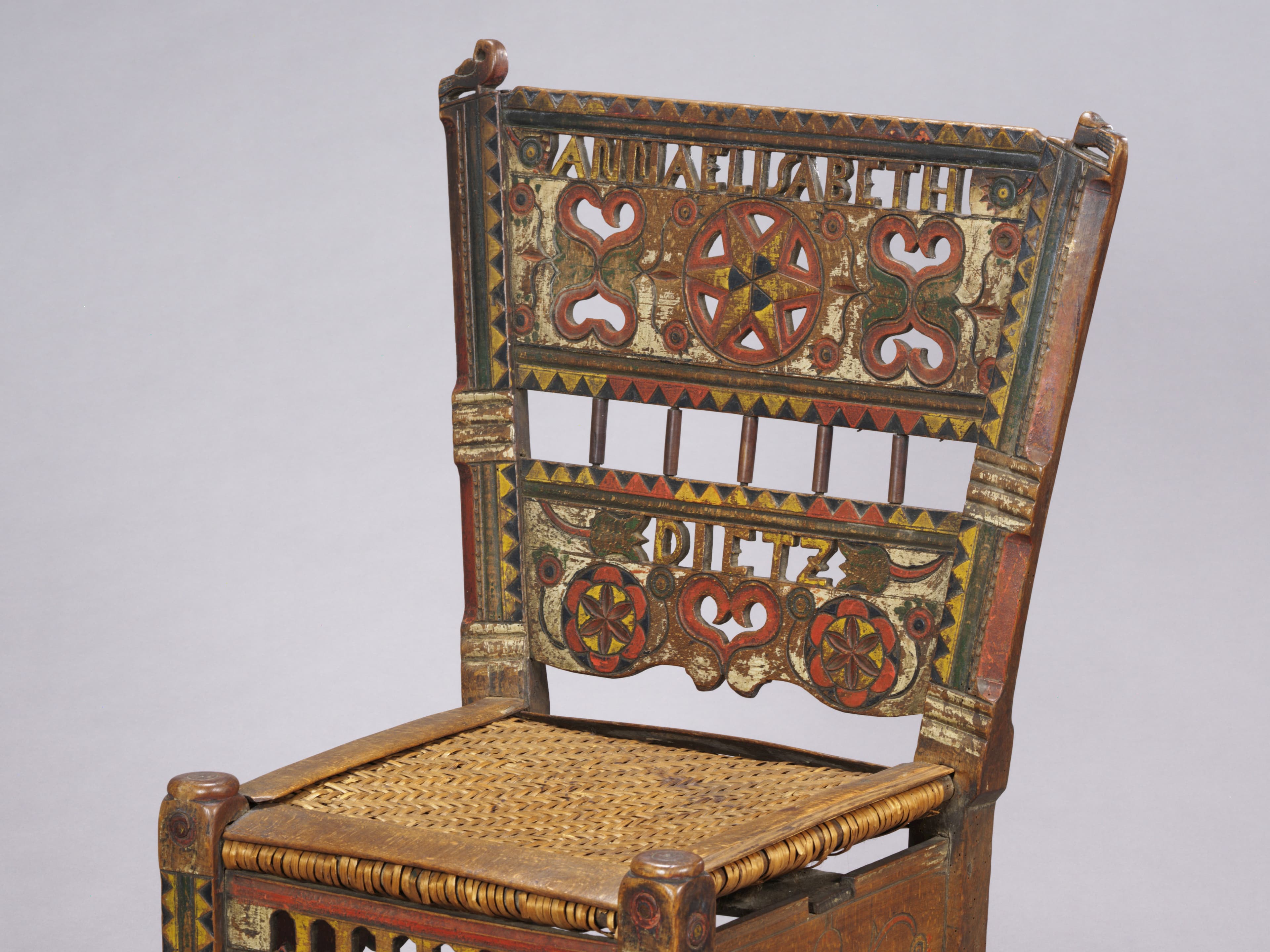 Antiker Holzstuhl mit komplizierten, farbenfrohen Volkskunstmustern und geflochtener Sitzfläche.
