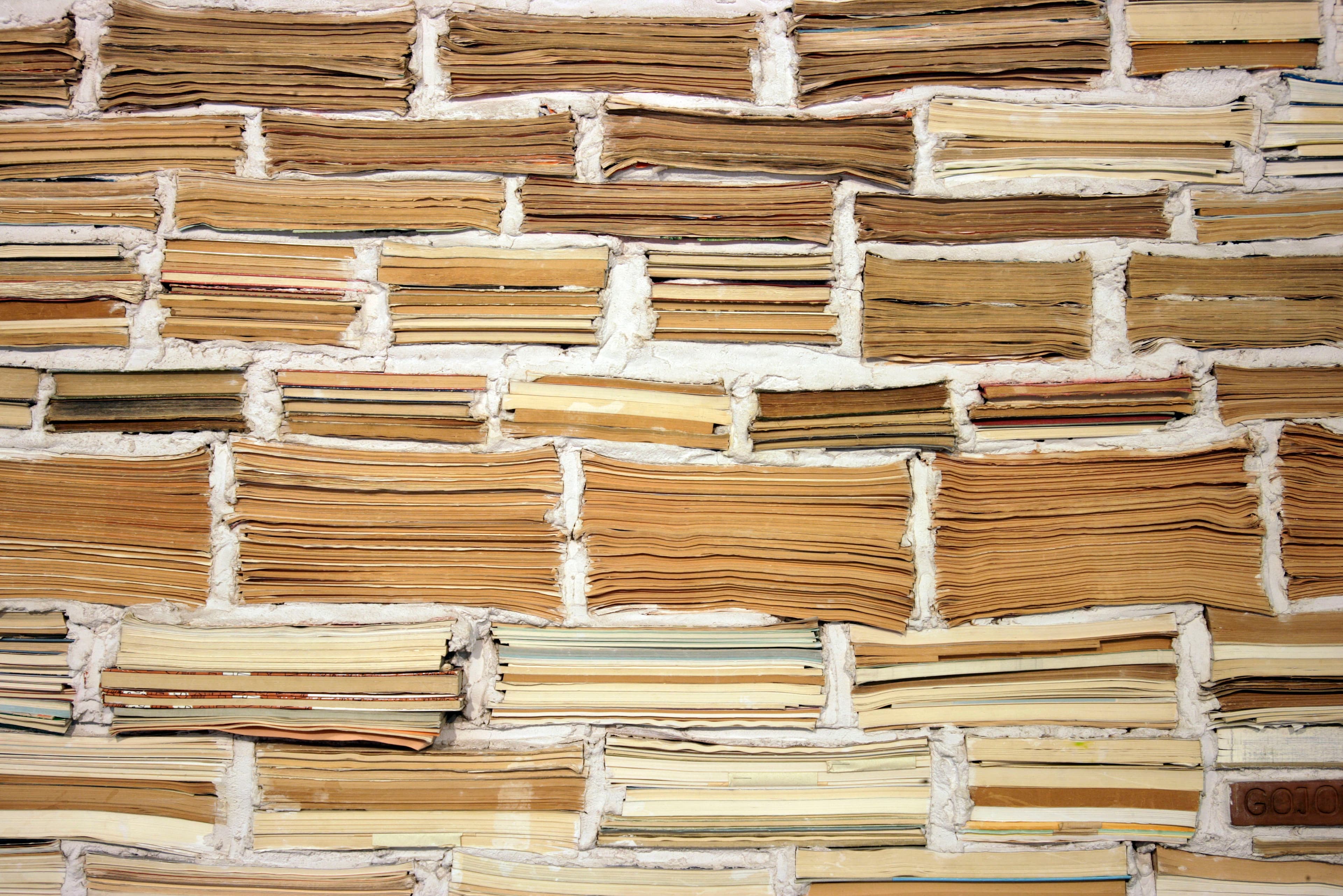 Stapel alter Bücher, die horizontal angeordnet sind, um einer Ziegelwand zu ähneln, wobei Buchrücken und Seiten ein strukturiertes Muster bilden.