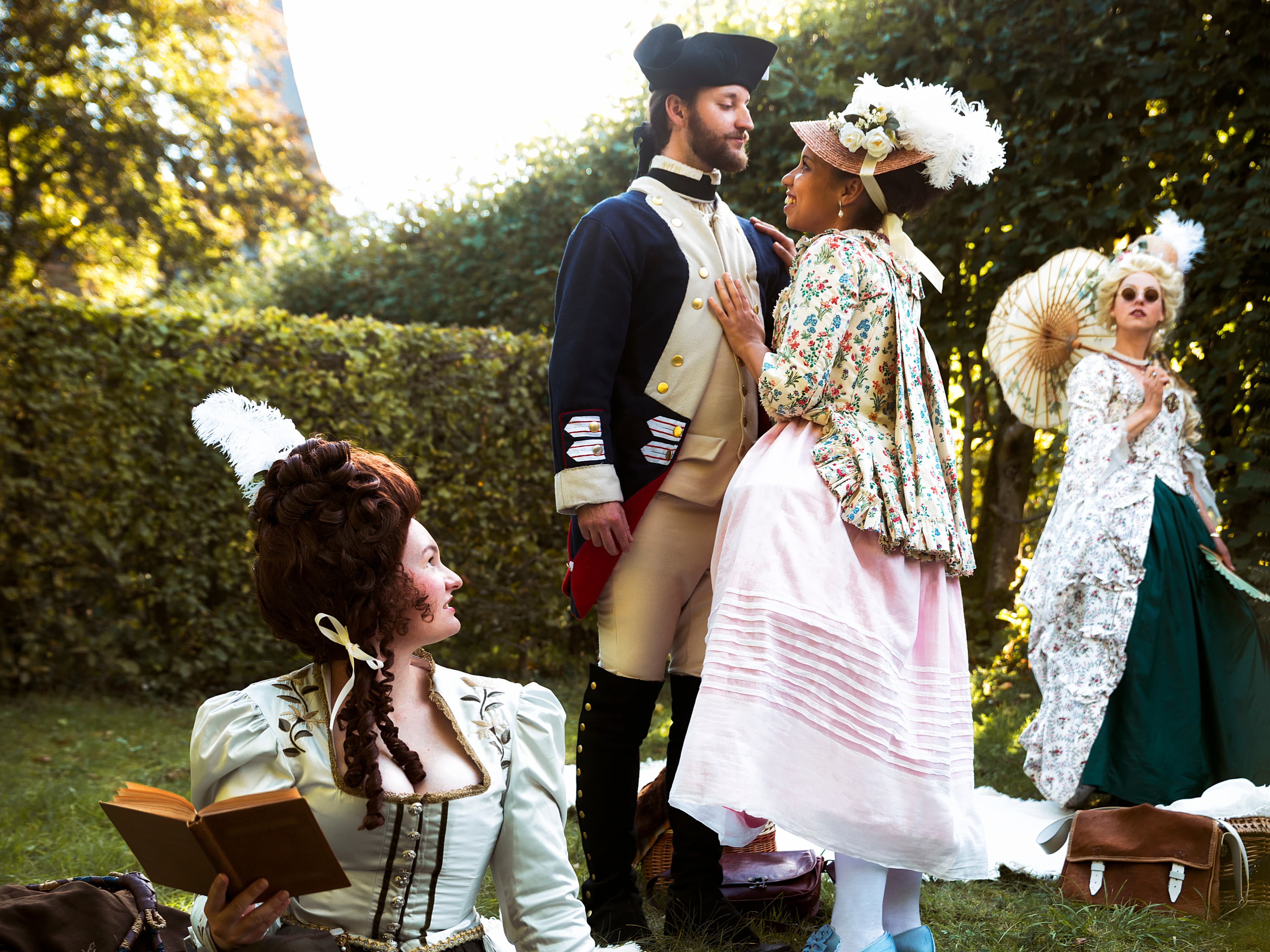 People in 18th-century attire in a garden; a man and woman stand together, another woman reads, and a third holds a parasol.
