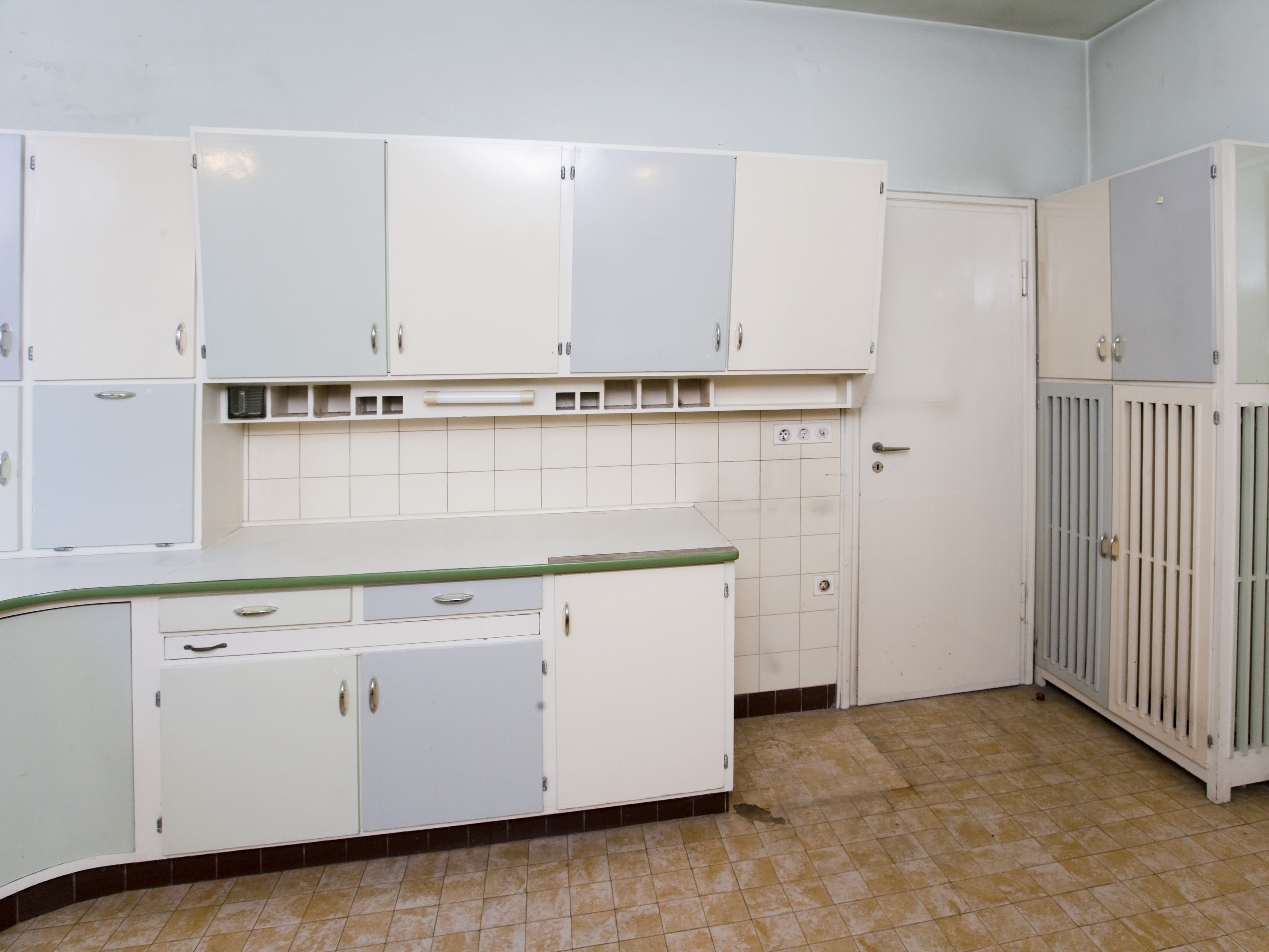 Eine Vintage-Küche mit hellblauen und weißen Schränken, gefliester Küchenrückwand und einem beigefarbenen Fliesenboden.