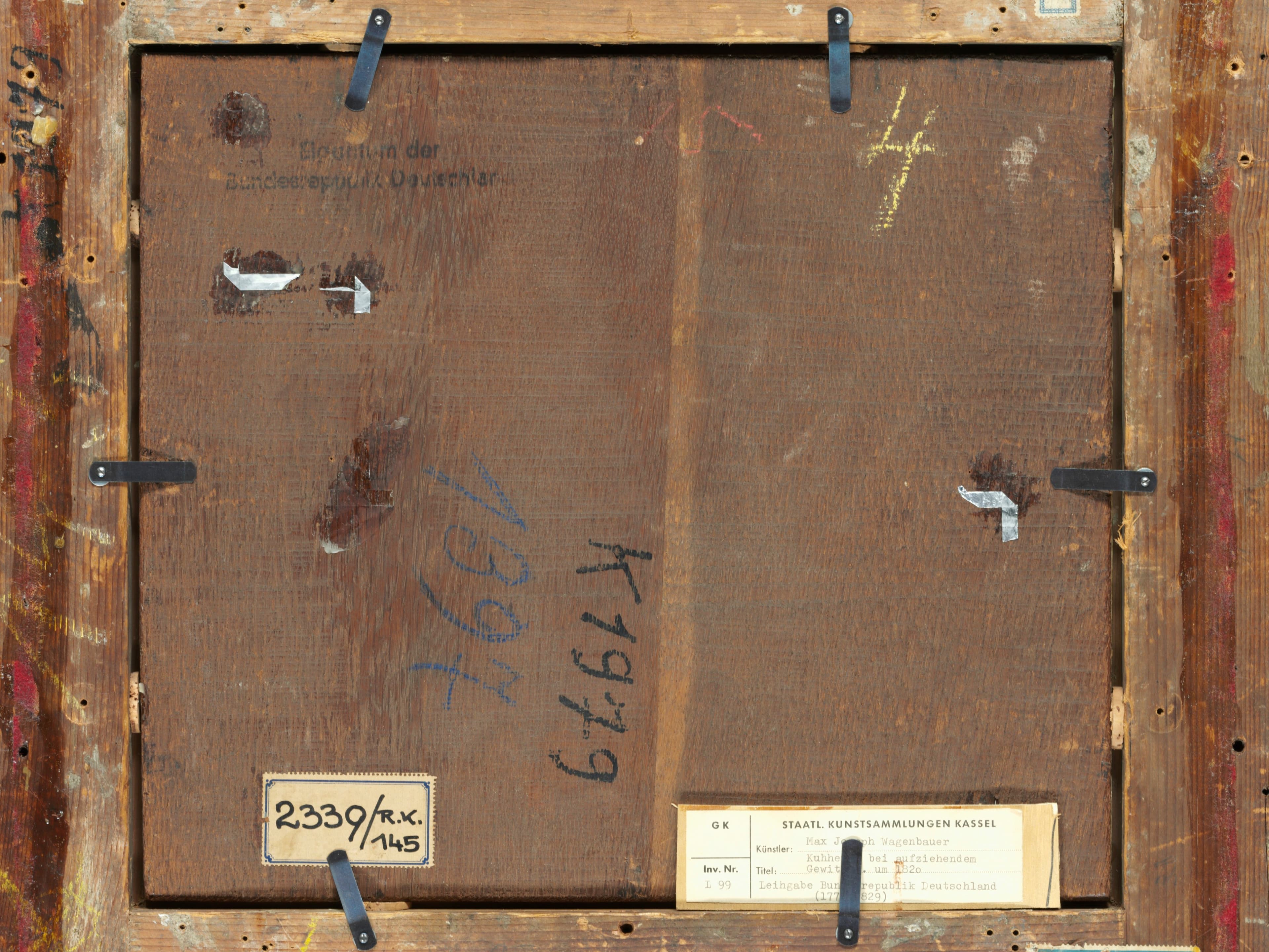 Die Rückseite eines gerahmten Kunstwerks mit Holzlatten, Metallklammern, verschiedenen Nummern und angebrachten Etiketten.