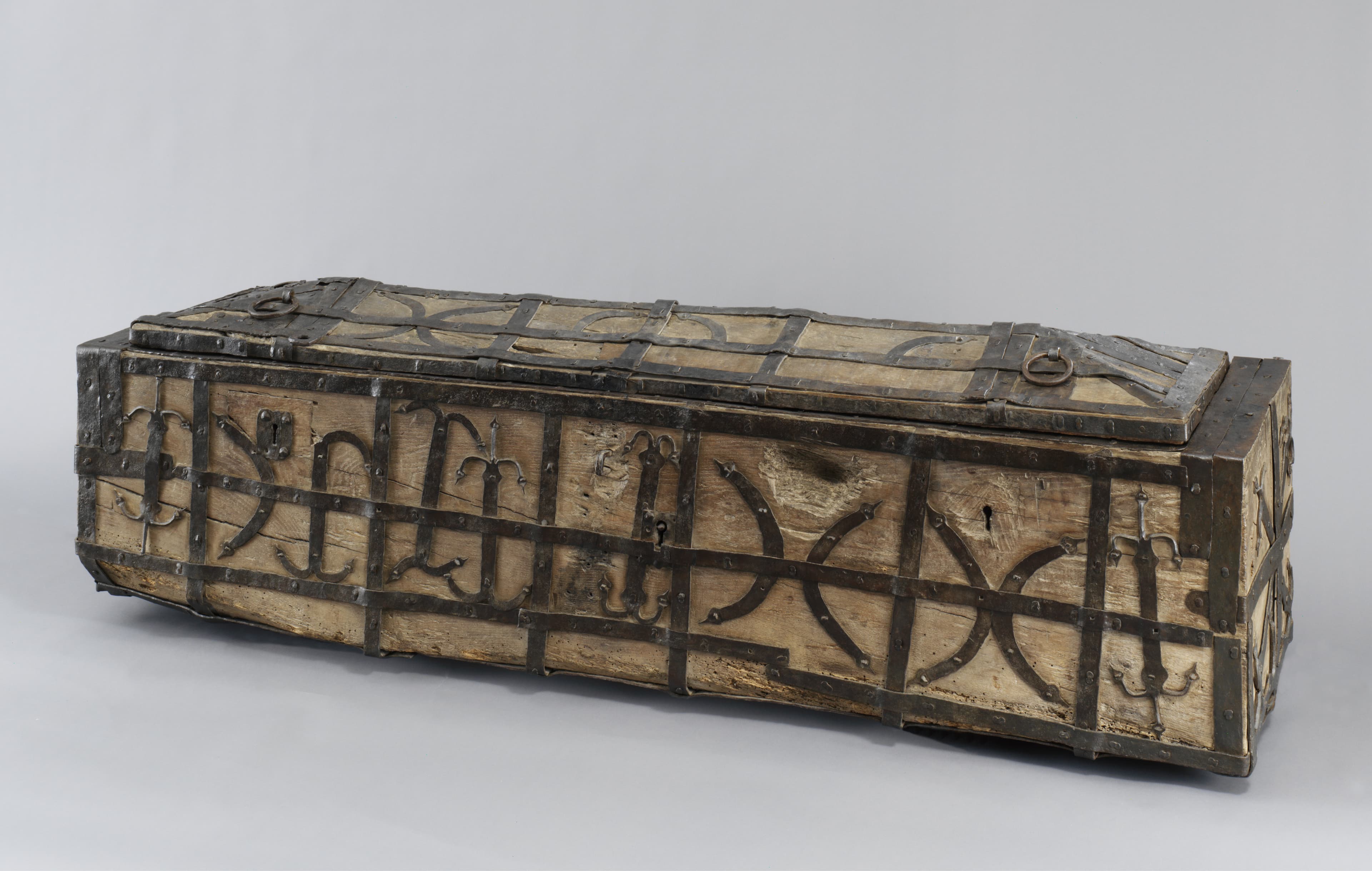 Eine rustikale Holztruhe mit Metallverstärkungen und dekorativen Mustern, die auf einem schlichten Hintergrund ruht.