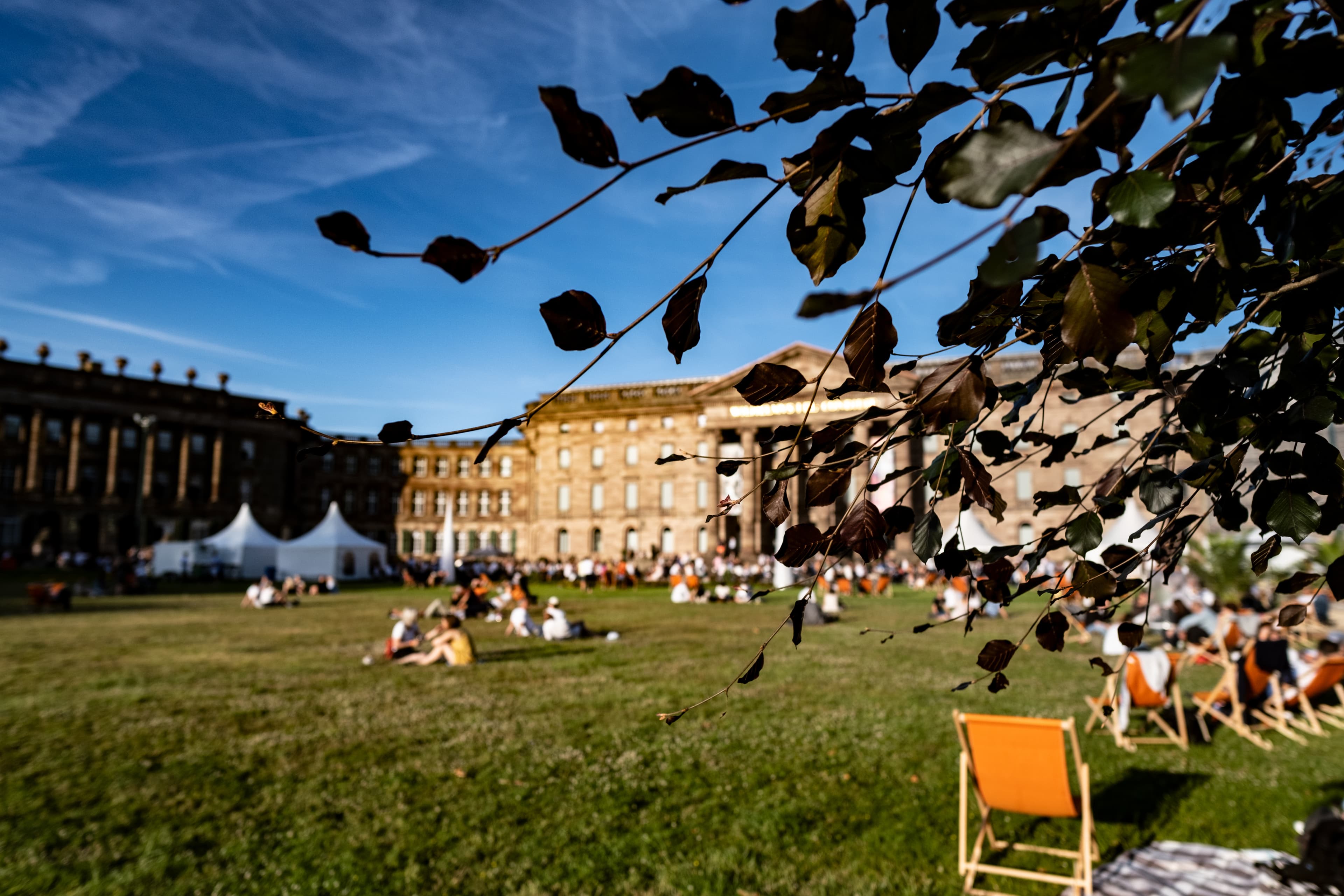 Menschen und Zelte vor Schloss Wilhelmshöhe, im Vordergrund Äste eines Baumes.