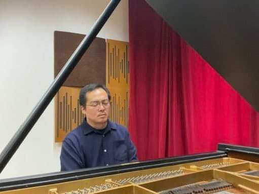 Person, die in einem Raum mit Akustikplatten und roten Vorhängen einen Flügel spielt und sich auf die Musik konzentriert.