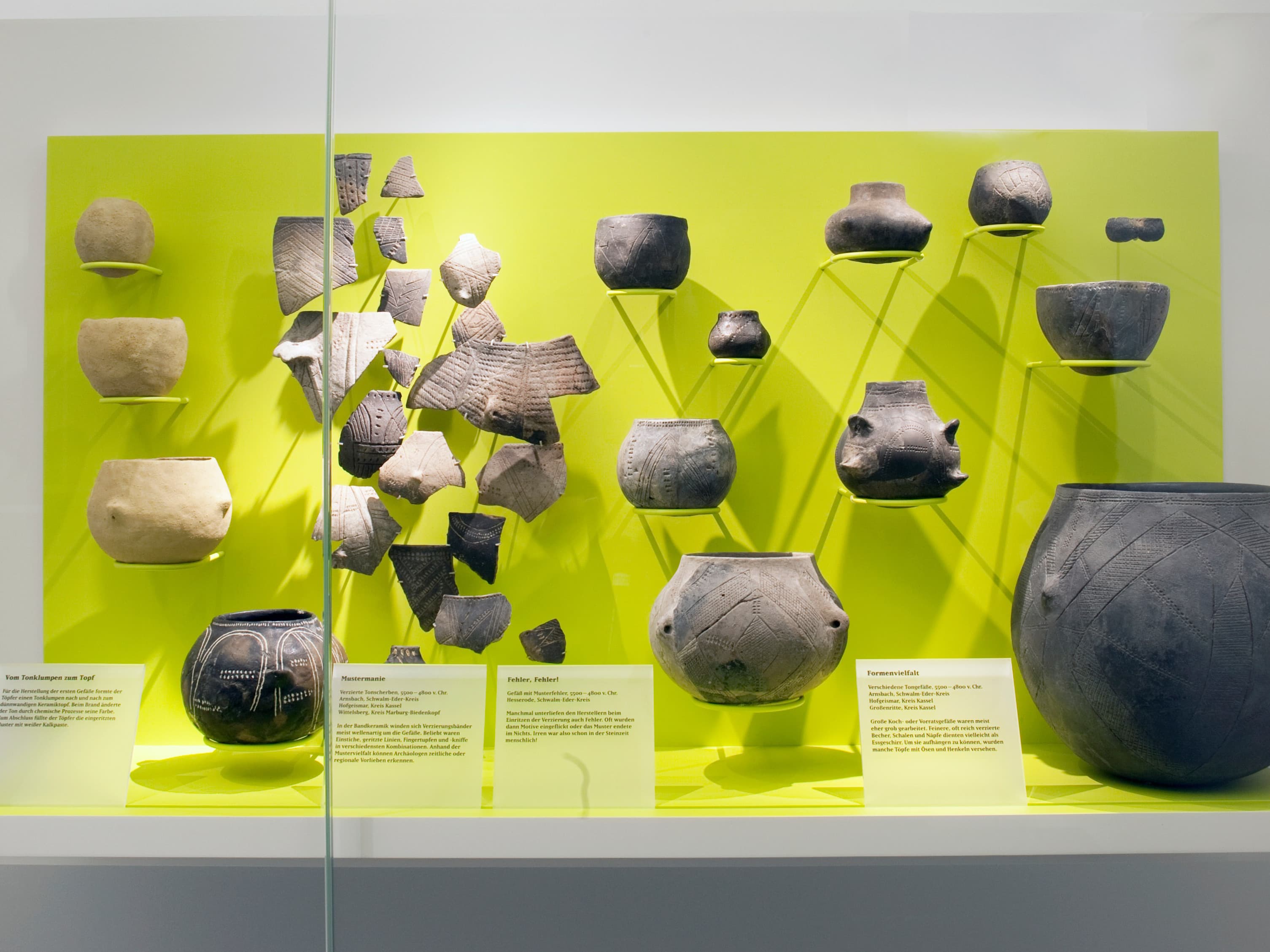 Ausstellung antiker Tonscherben und rekonstruierter Töpfe auf leuchtend gelbem Hintergrund in einer Museumsausstellung.