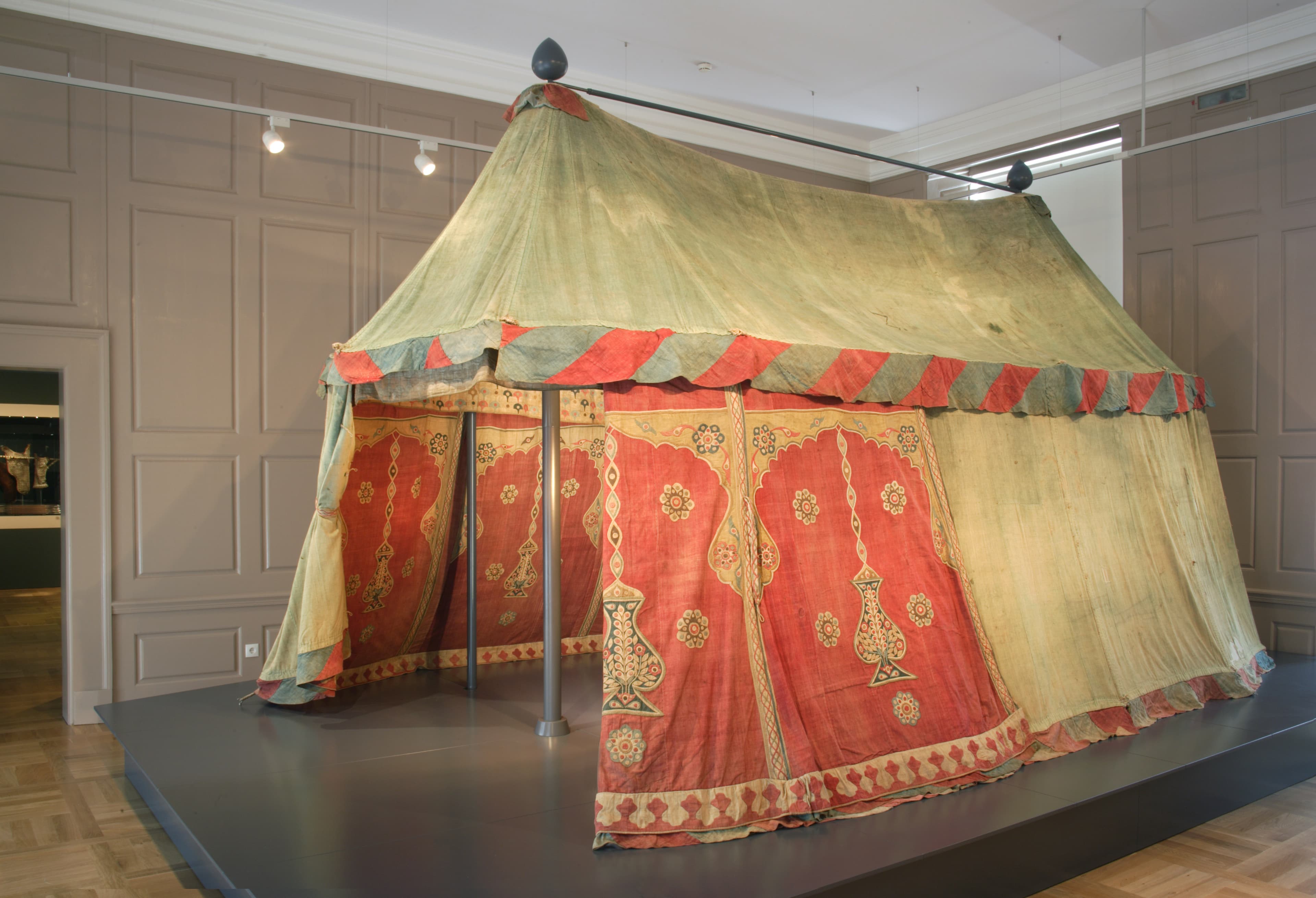 A historical tent with ornate red and gold patterns on display in a museum setting.