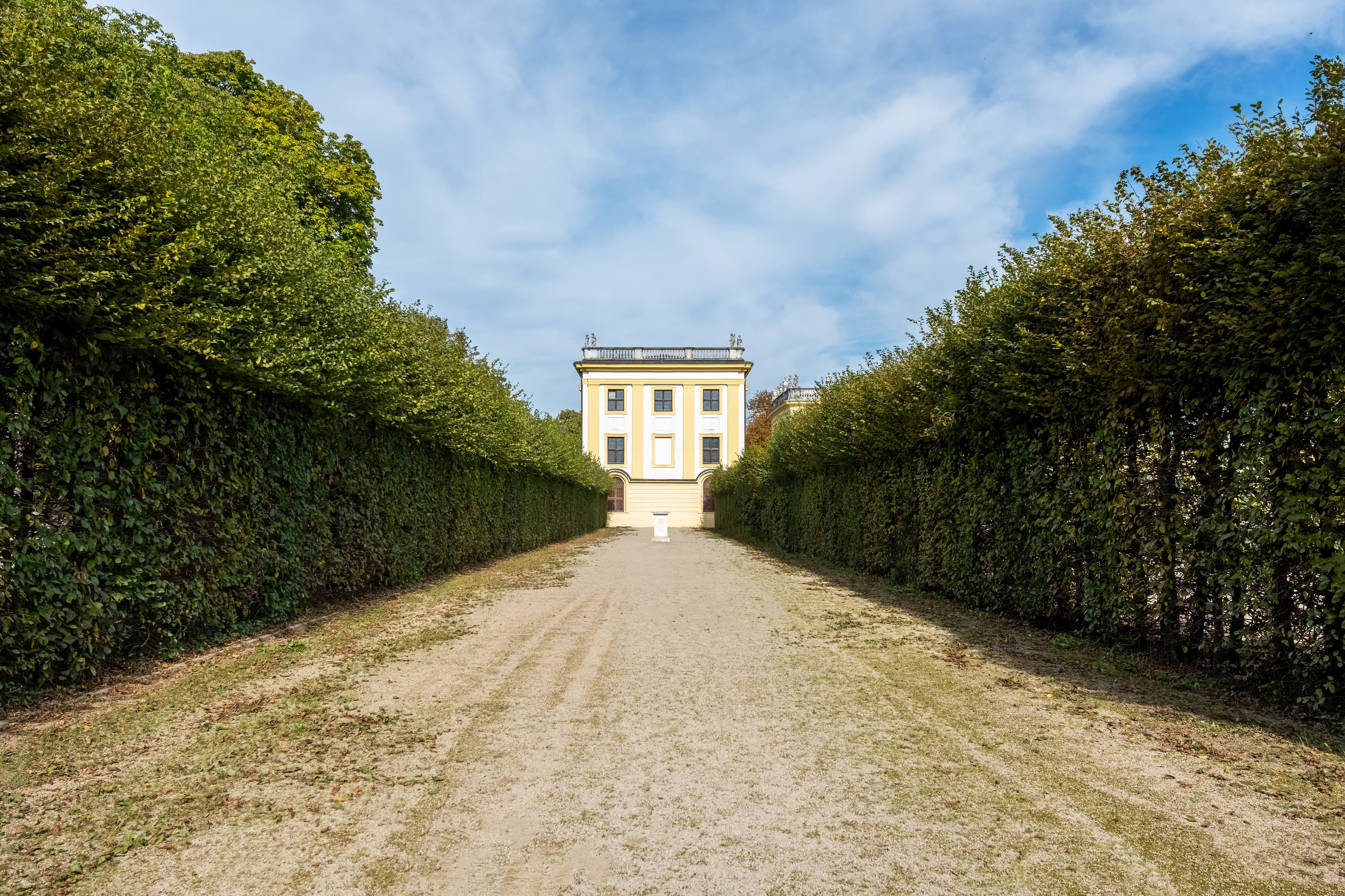 View across a wide corridor lined with high hedges to the marble bath