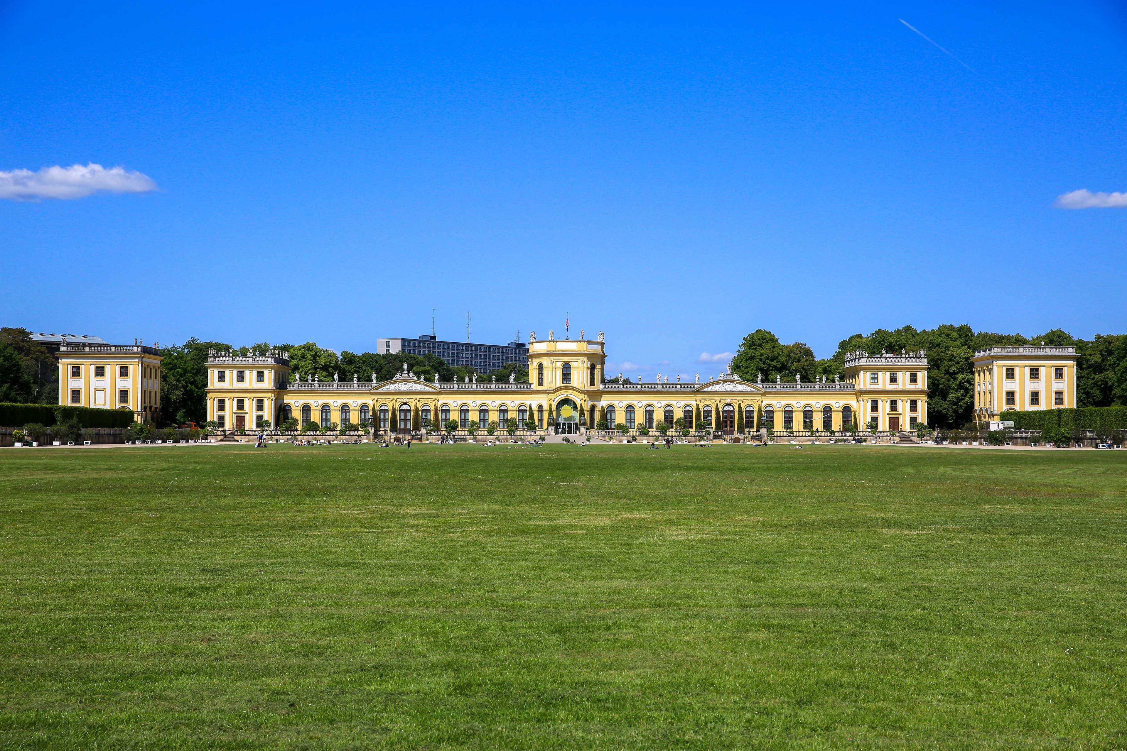 Ein großes, gelbes historisches Gebäude mit Bogenfenstern und einem gepflegten Rasen unter einem klaren blauen Himmel.