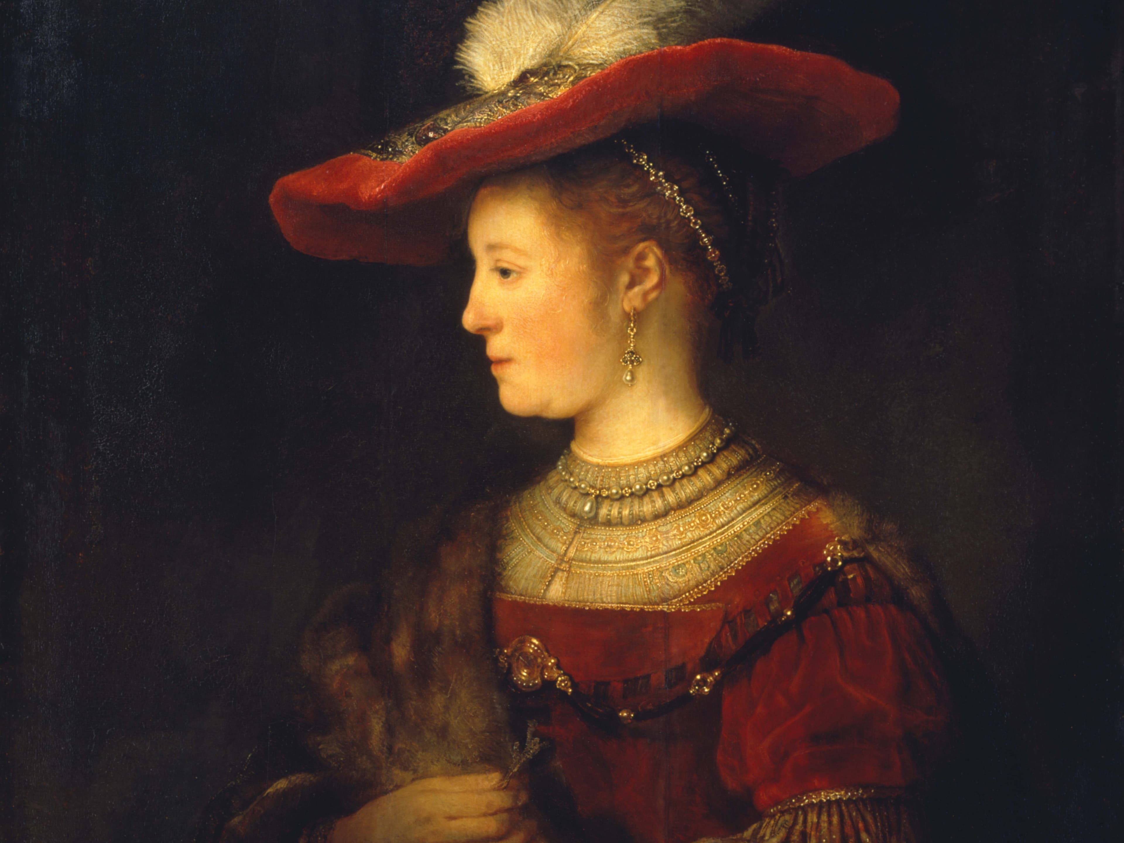 A woman in a red dress and ornate hat with a feather, adorned with jewelry, gazes to the side against a dark background.